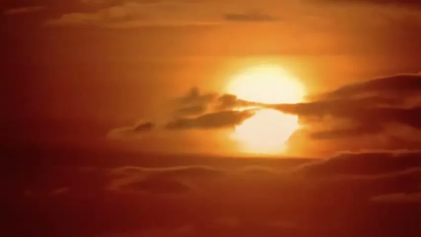 The sun, a bright orange orb, is partially obscured by dark clouds in a wide shot of the sky.