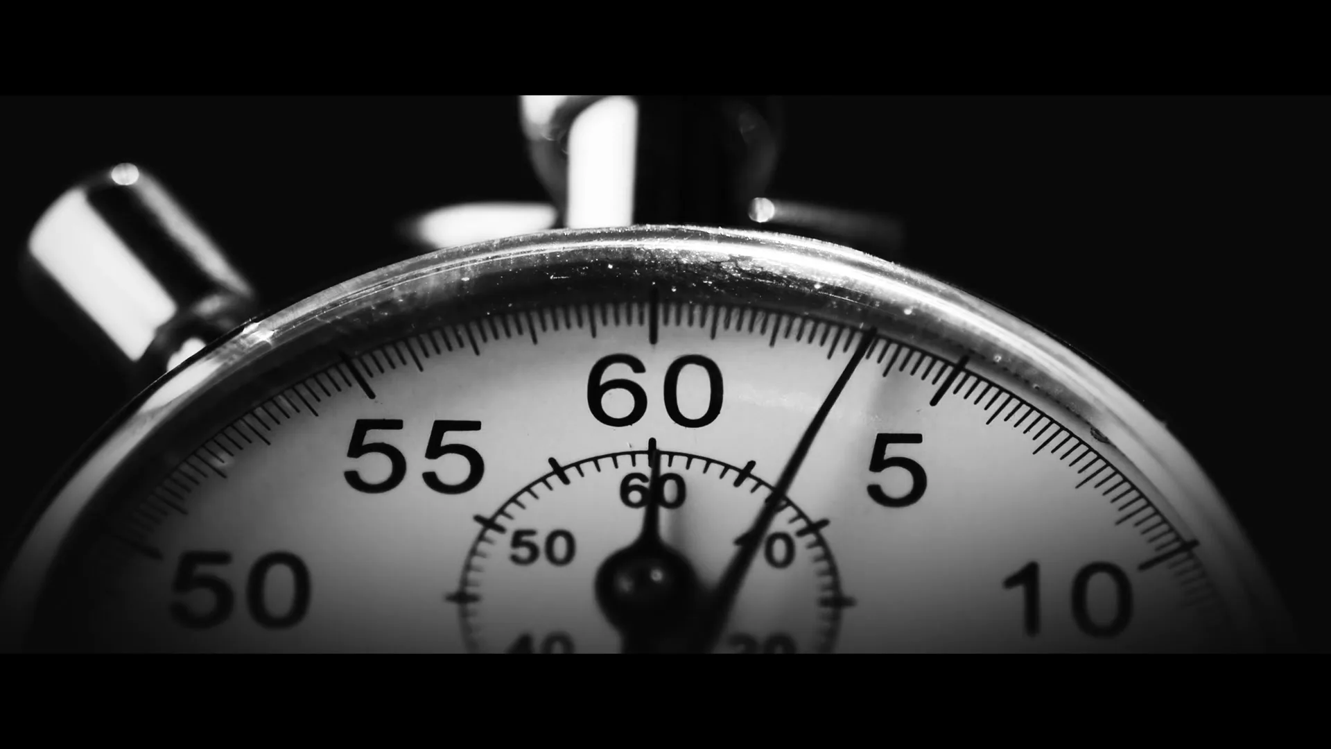 A close-up shot of a stopwatch in black and white, with the second hand ticking past the 5-second mark on a dark background.