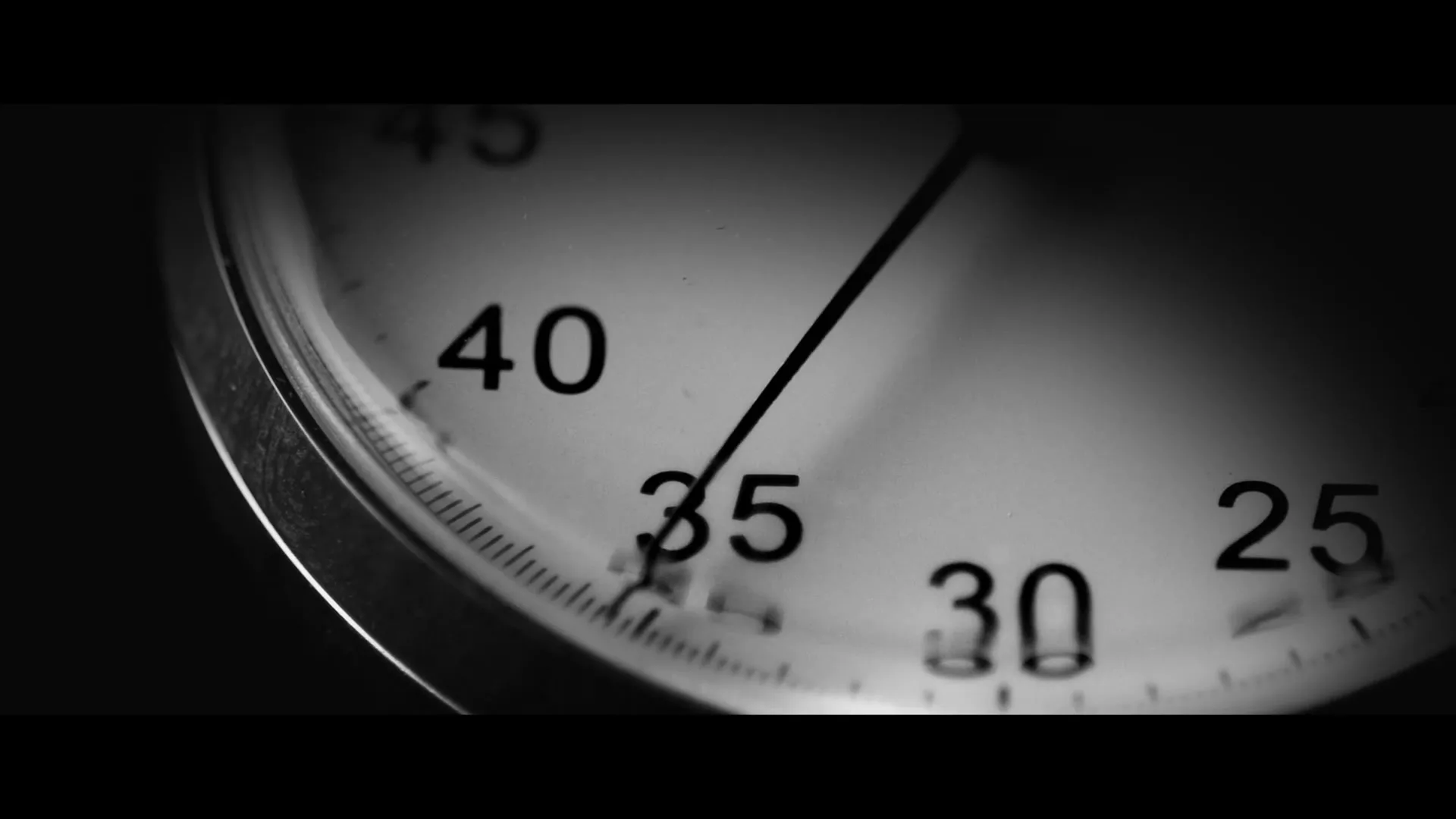 A close-up, black and white shot of a stopwatch face with the second hand ticking, emphasizing the passage of time.