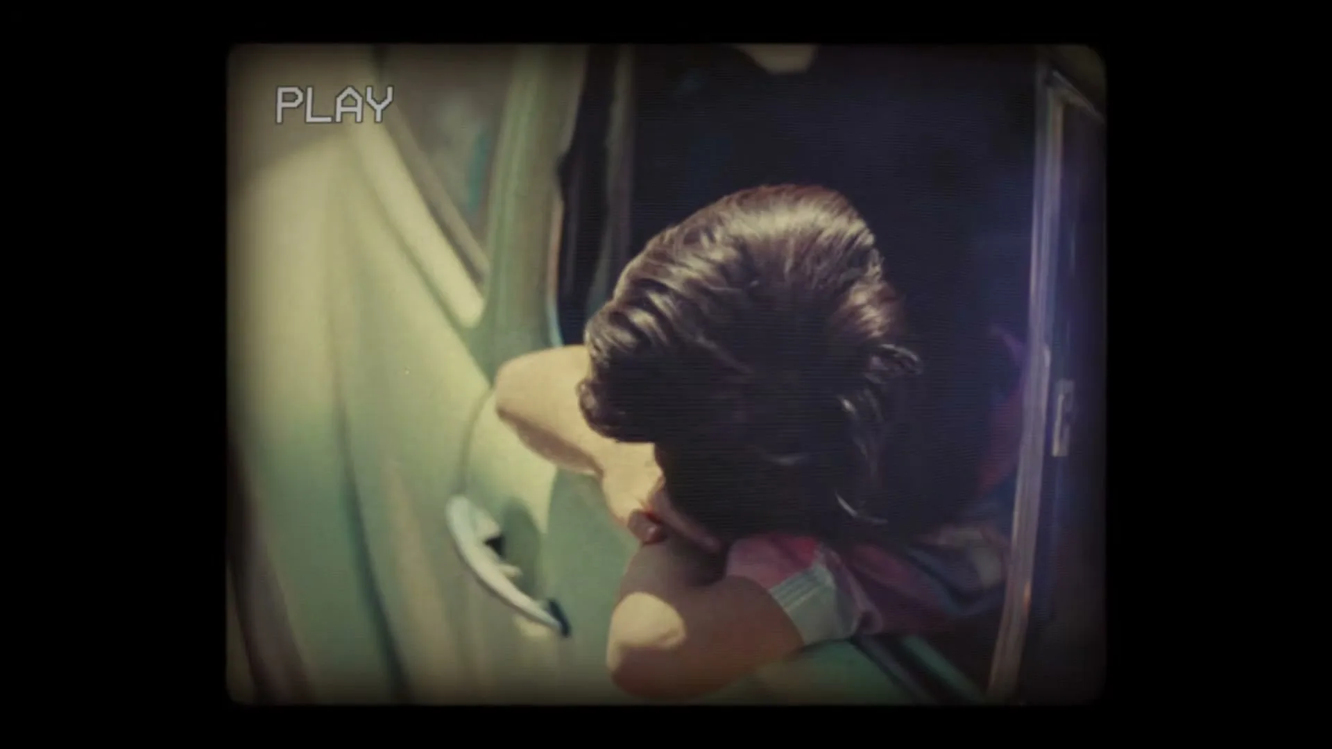 A woman with dark hair in a vintage car, seen from above, leans out the window, captured with a retro camcorder effect.