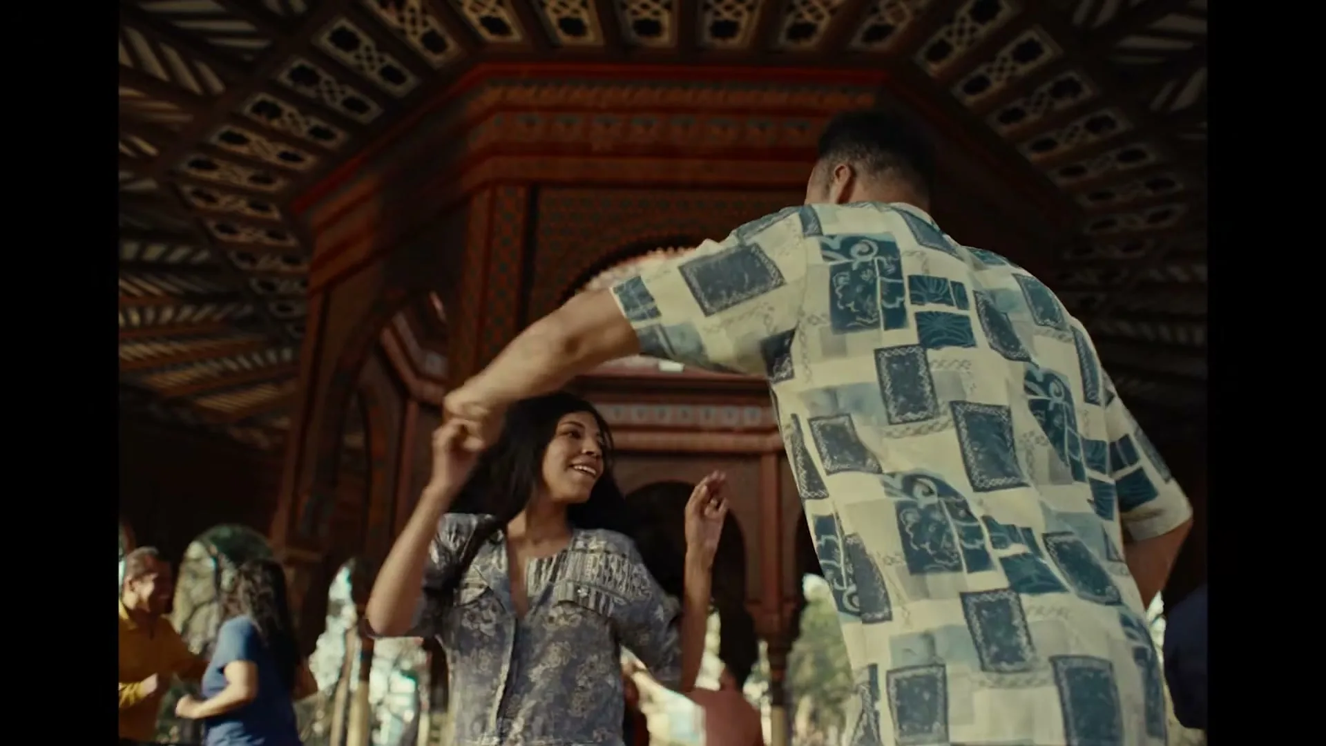 A man and a woman dance together in a beautiful, ornate building with intricate patterns and arches, surrounded by other people.