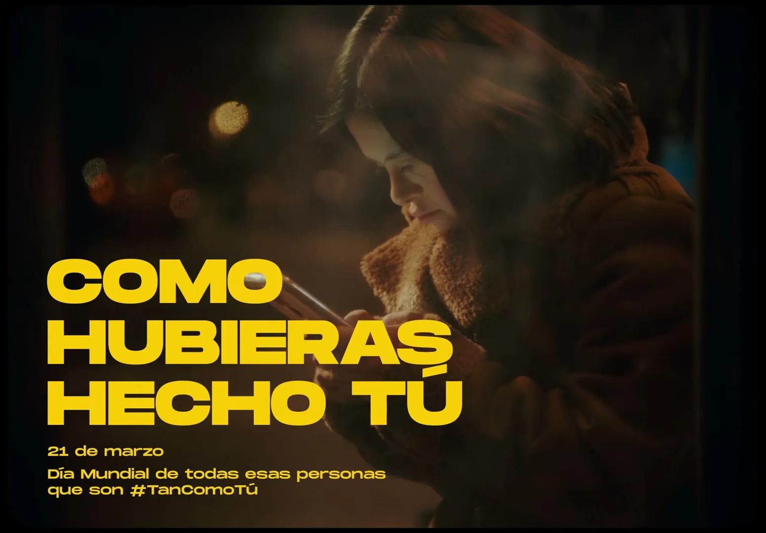 A young woman with brown hair and a brown coat looks down at her phone, sitting in a bus stop at night, with yellow text overlayed.