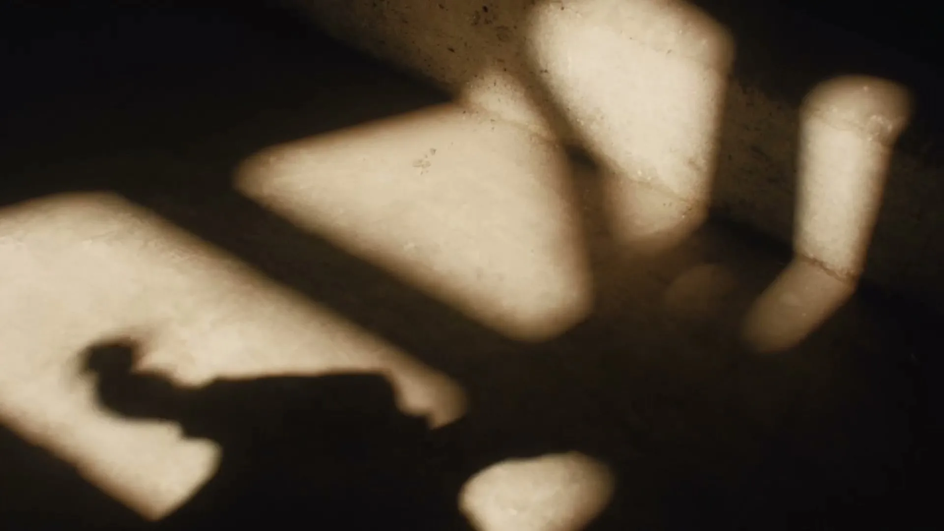 Sunlight streams through a window, casting abstract shapes and a person's shadow onto a textured floor, creating a play of light and dark.