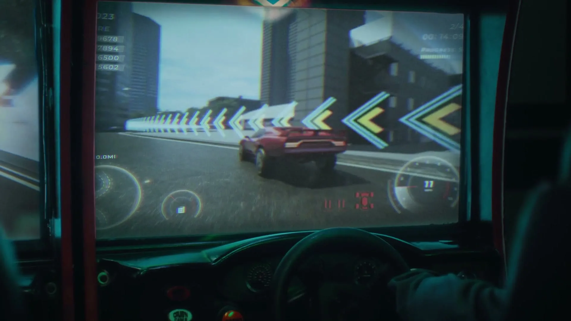 A person's hands are on the steering wheel of an arcade racing game, showing a red car on a city track.