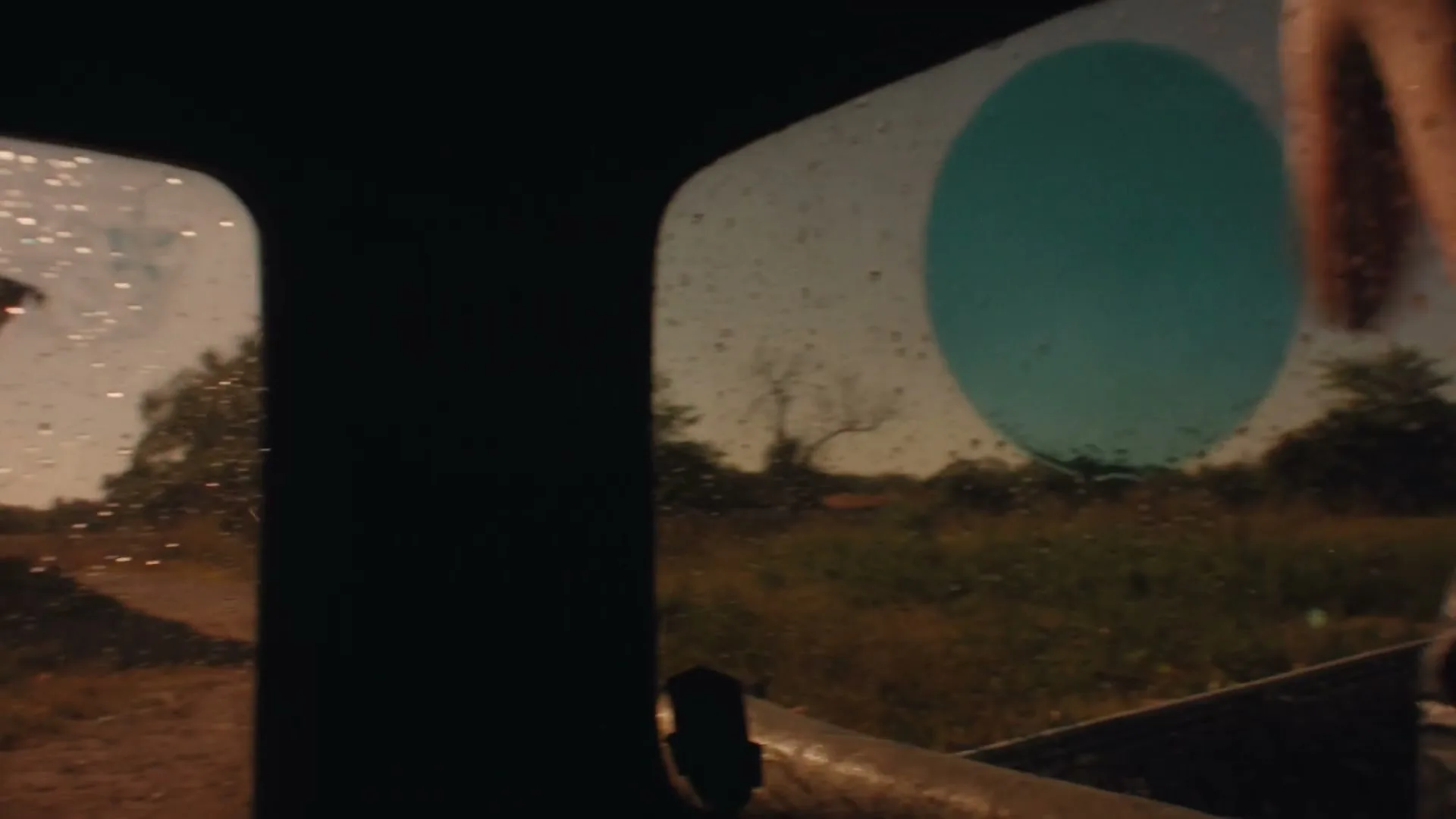 A young man, wet and shirtless, throws a blue water balloon from the back of a moving truck on a sunny day.