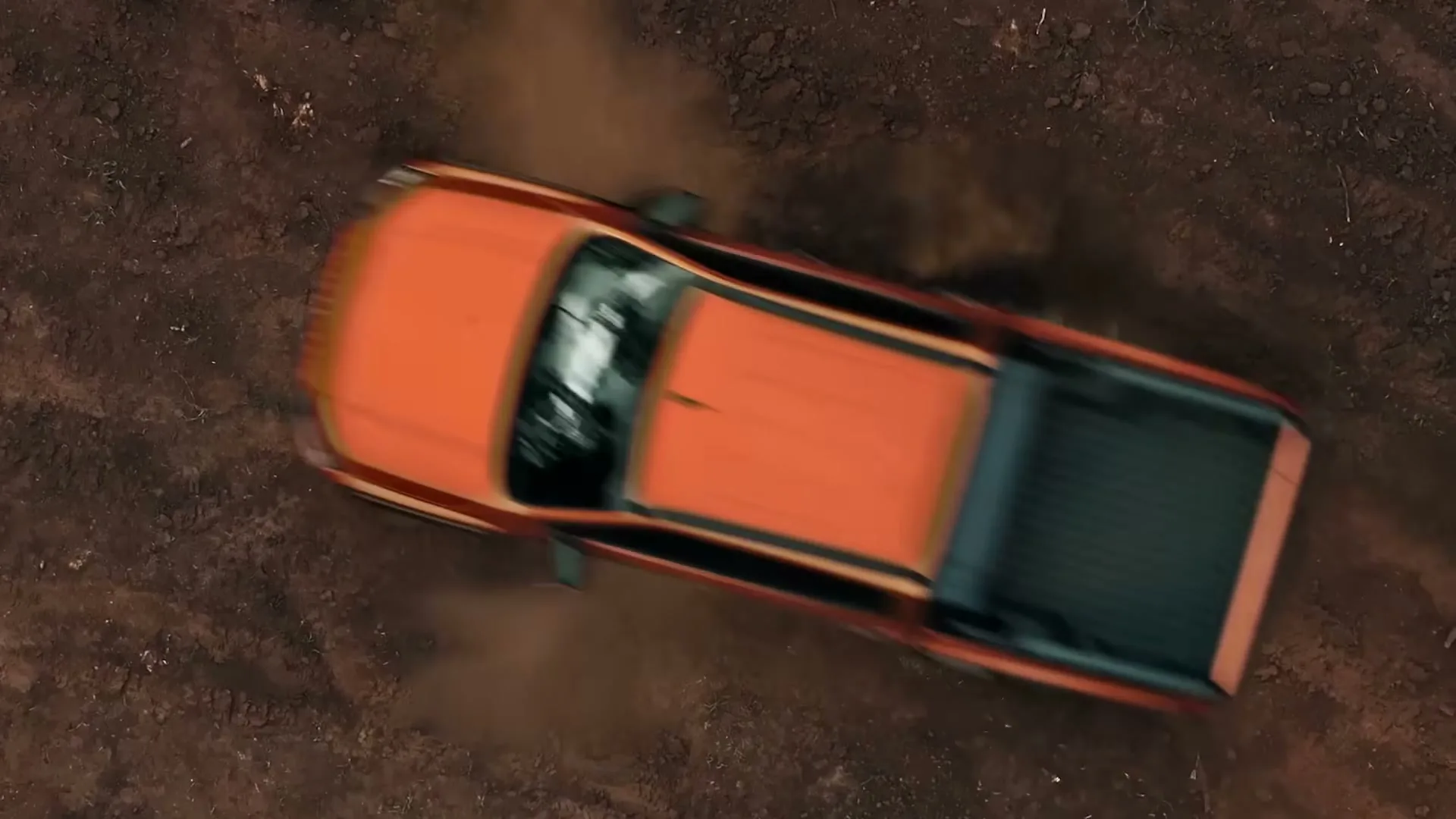 An orange Mitsubishi Triton drives over a dirt road, kicking up dust and revealing the words "THE ALL NEW MITSUBISHI TRITON" carved into the ground.