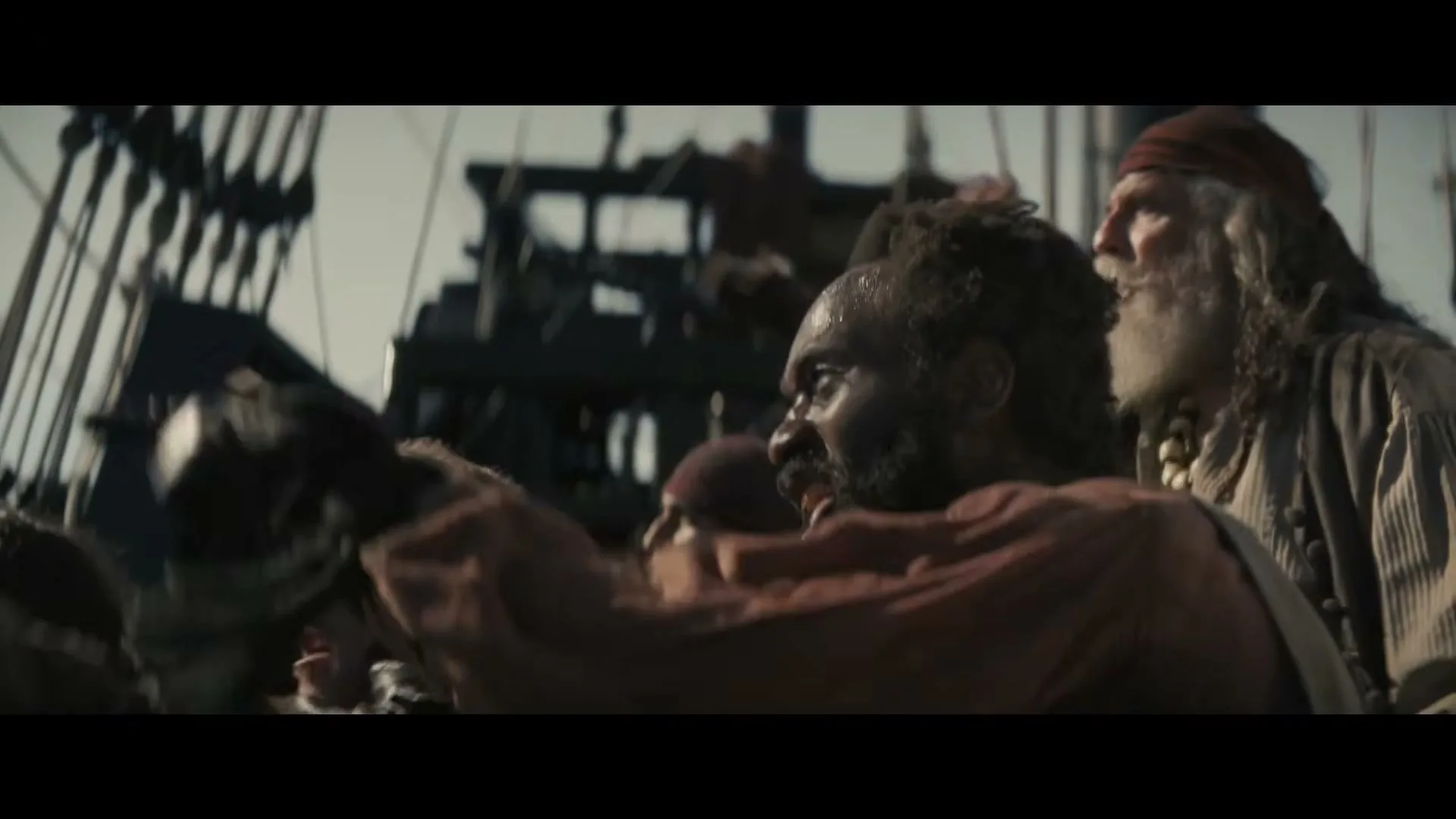 A group of pirates, including a Black man with a beard and a white man with an eyepatch, are yelling and fighting on a ship's deck during the day.