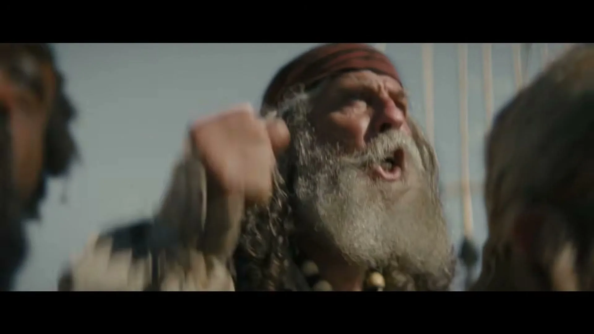 A male pirate with a long white beard and a red bandana shouts, surrounded by other pirates on a ship's deck under a bright sky.