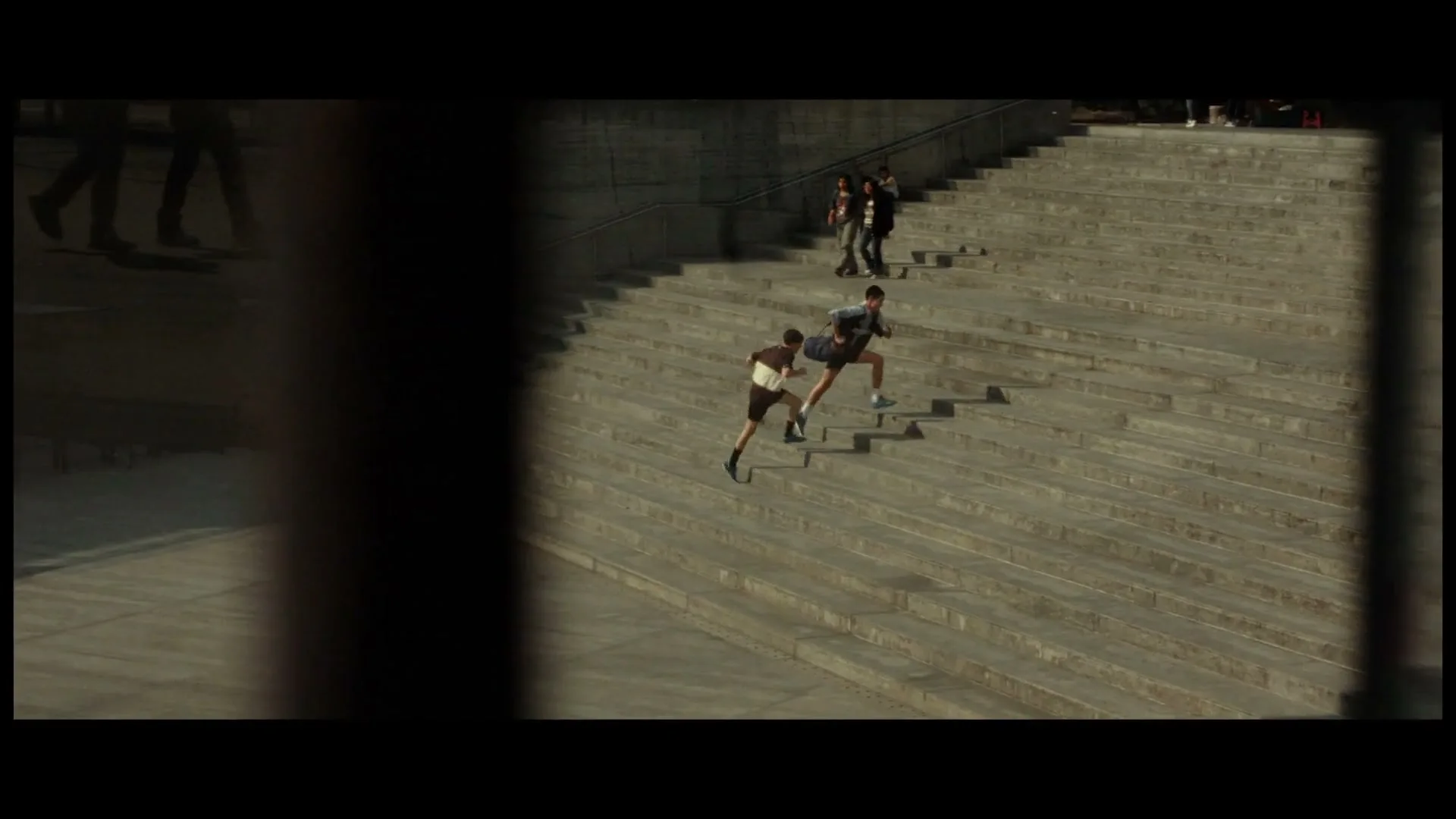 Two young men in athletic wear run up a wide, concrete staircase, while other people walk further up the stairs in an urban setting.