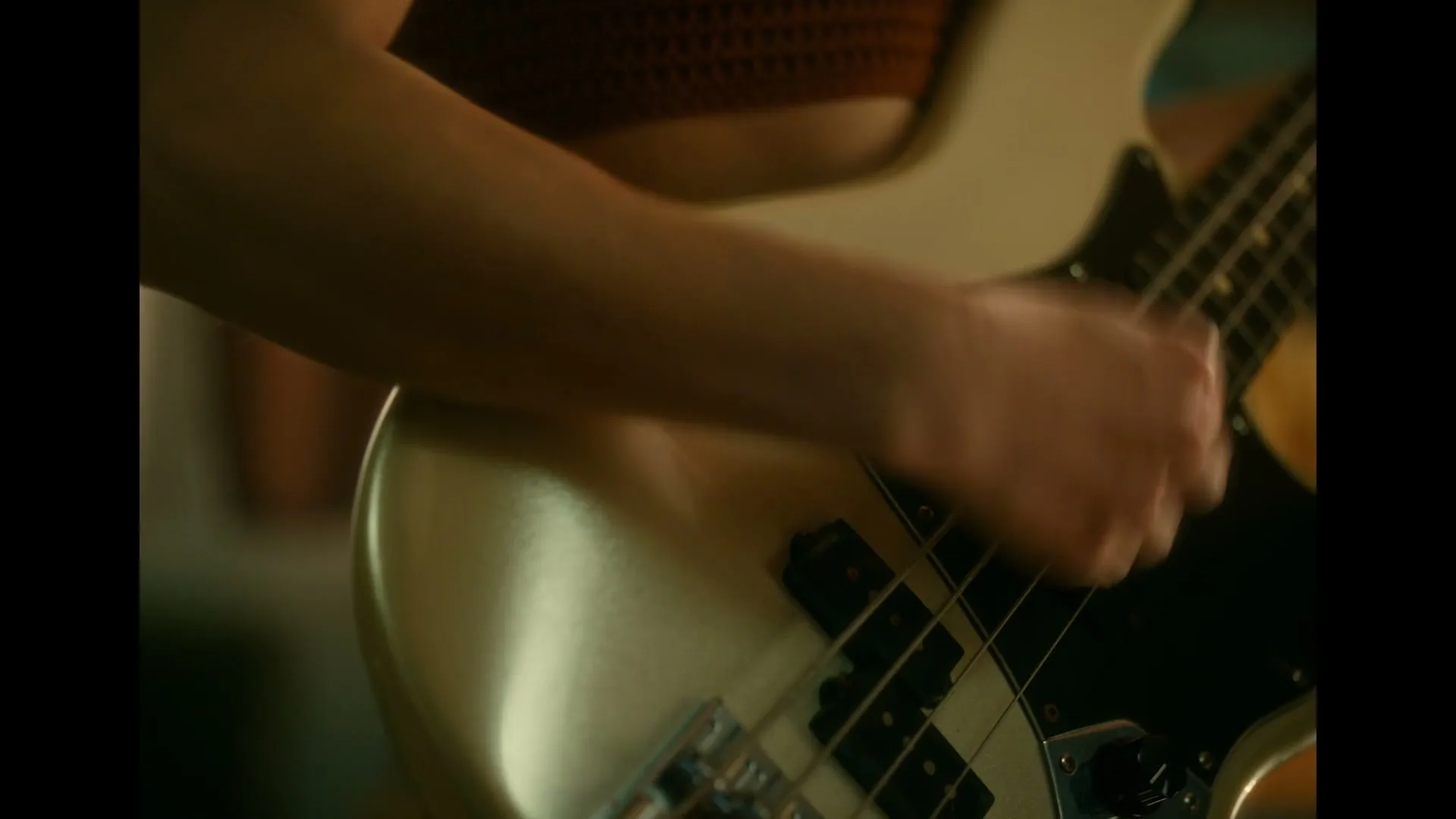 A person's arm and hand are seen playing a bass guitar, with the instrument's body and strings in focus.