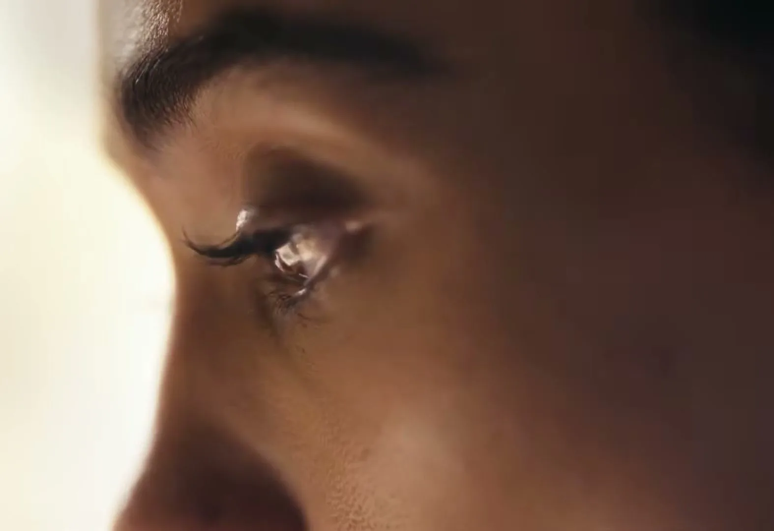A close-up of a person's eye, with a tear welling up, suggesting deep emotion or sadness.
