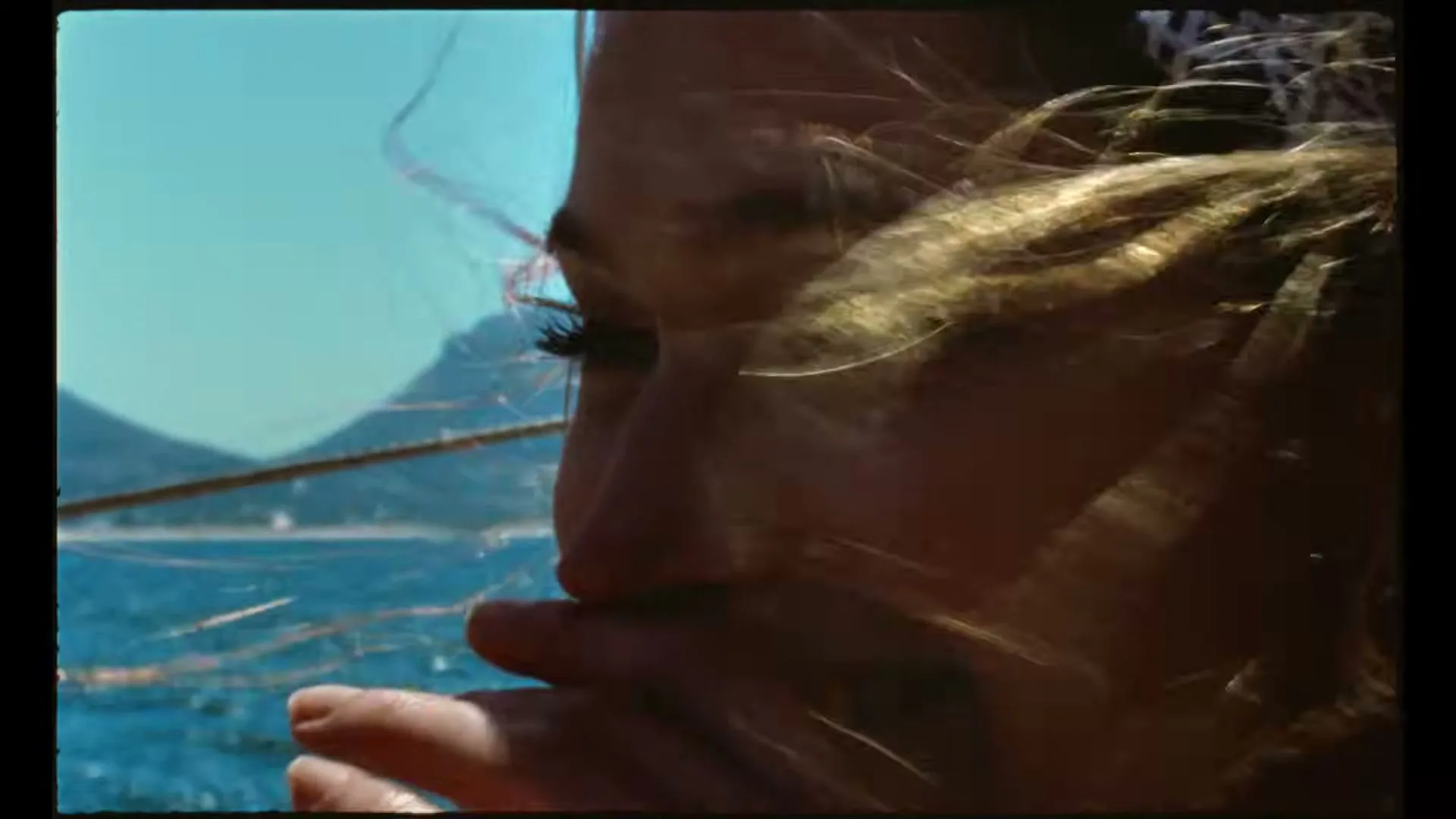A young woman with long blonde hair smiles, looking out at the ocean from a boat on a sunny day.