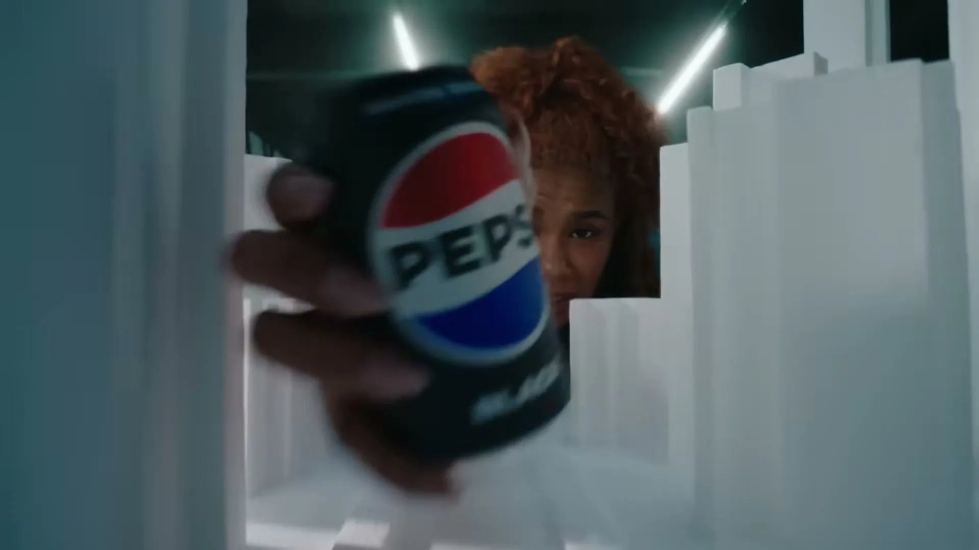 A woman with curly red hair reaches into a miniature city model to grab a can of Pepsi Black.