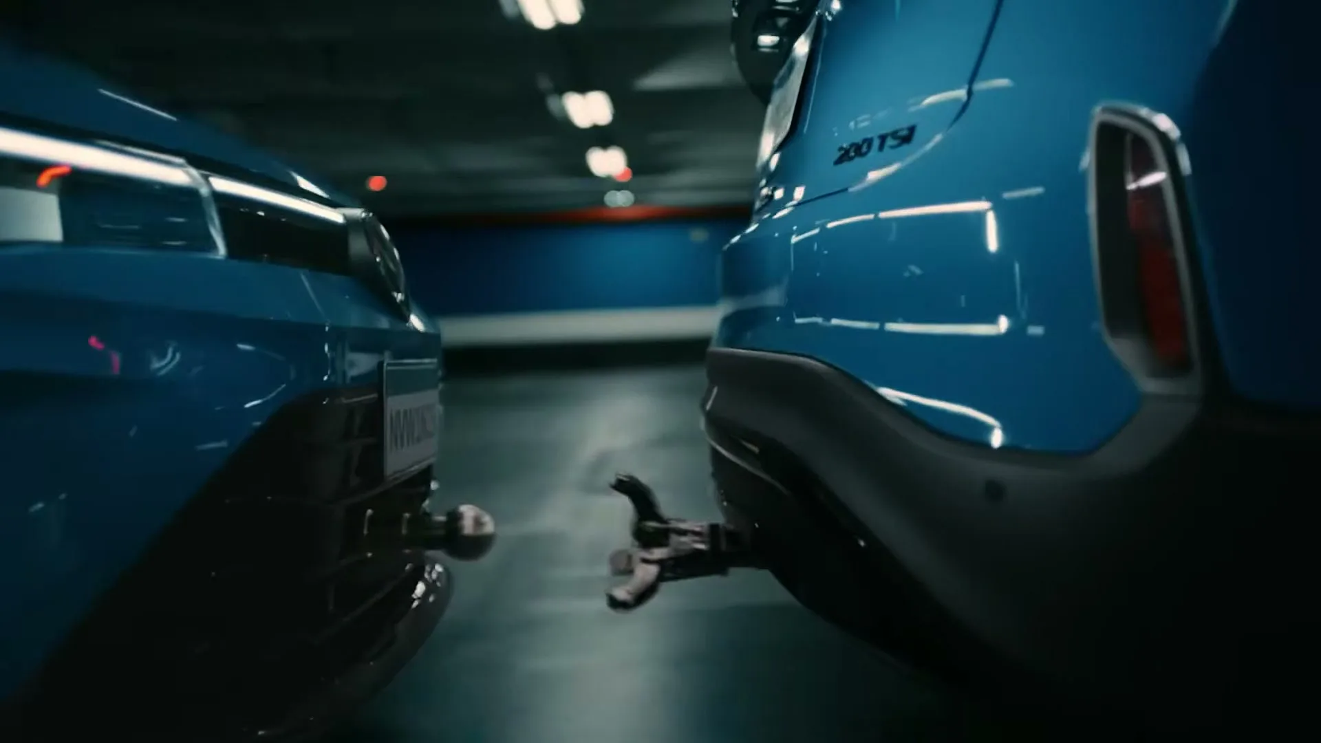 Two blue Volkswagen cars, one with a tow hitch, connect in a dark, empty underground parking garage.