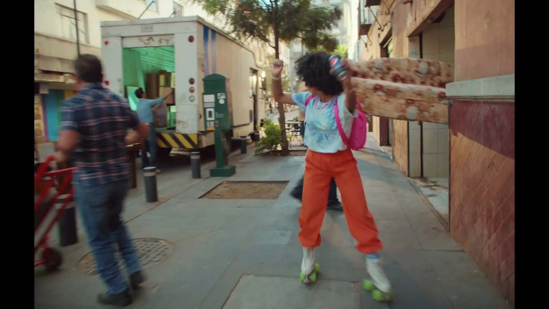 A young woman with an afro and roller skates dances down a busy city sidewalk as people move furniture and boxes.