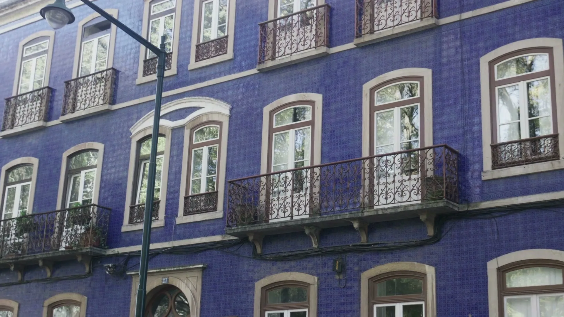 A blue tiled building with multiple windows and balconies is shown from a slightly low angle, with a street lamp in the foreground.