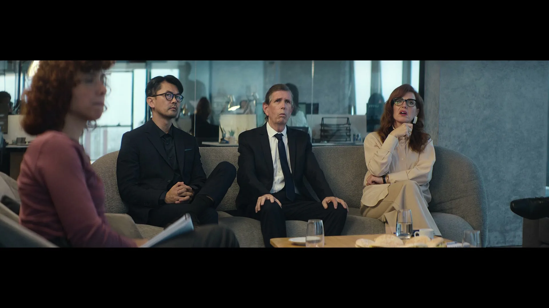 Four people, three of whom are seated on a couch, listen intently in a modern office setting.