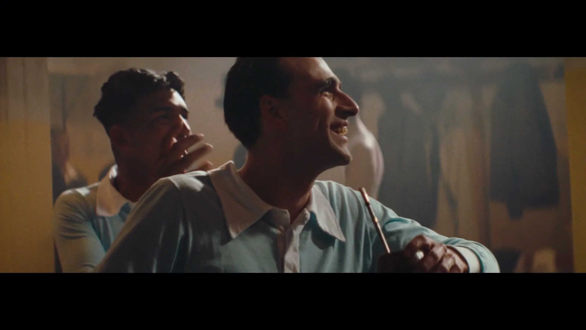 Two male soccer players in light blue jerseys laugh and celebrate in a dimly lit locker room.