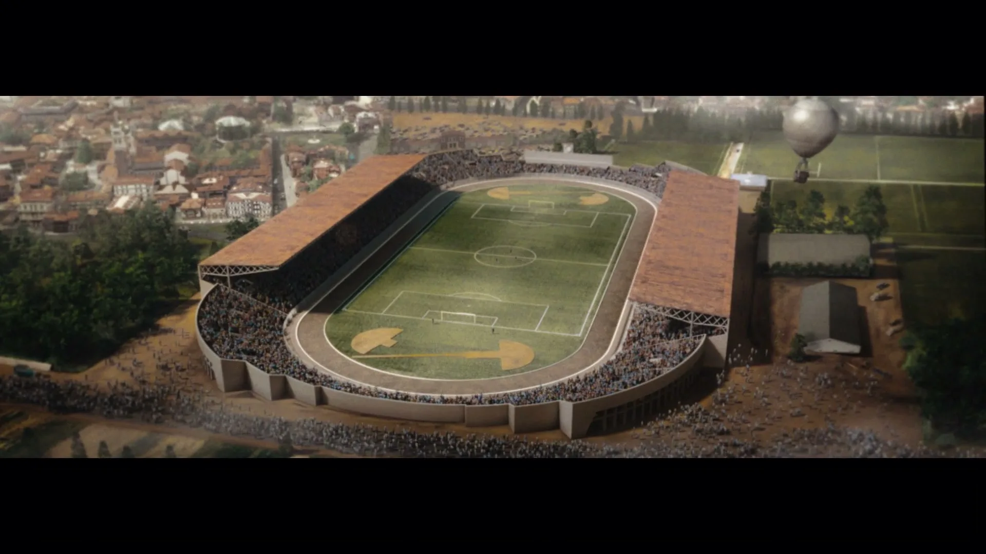 An aerial view of a large, old-fashioned stadium with a soccer field and running track, surrounded by a town and trees, under a bright sky.
