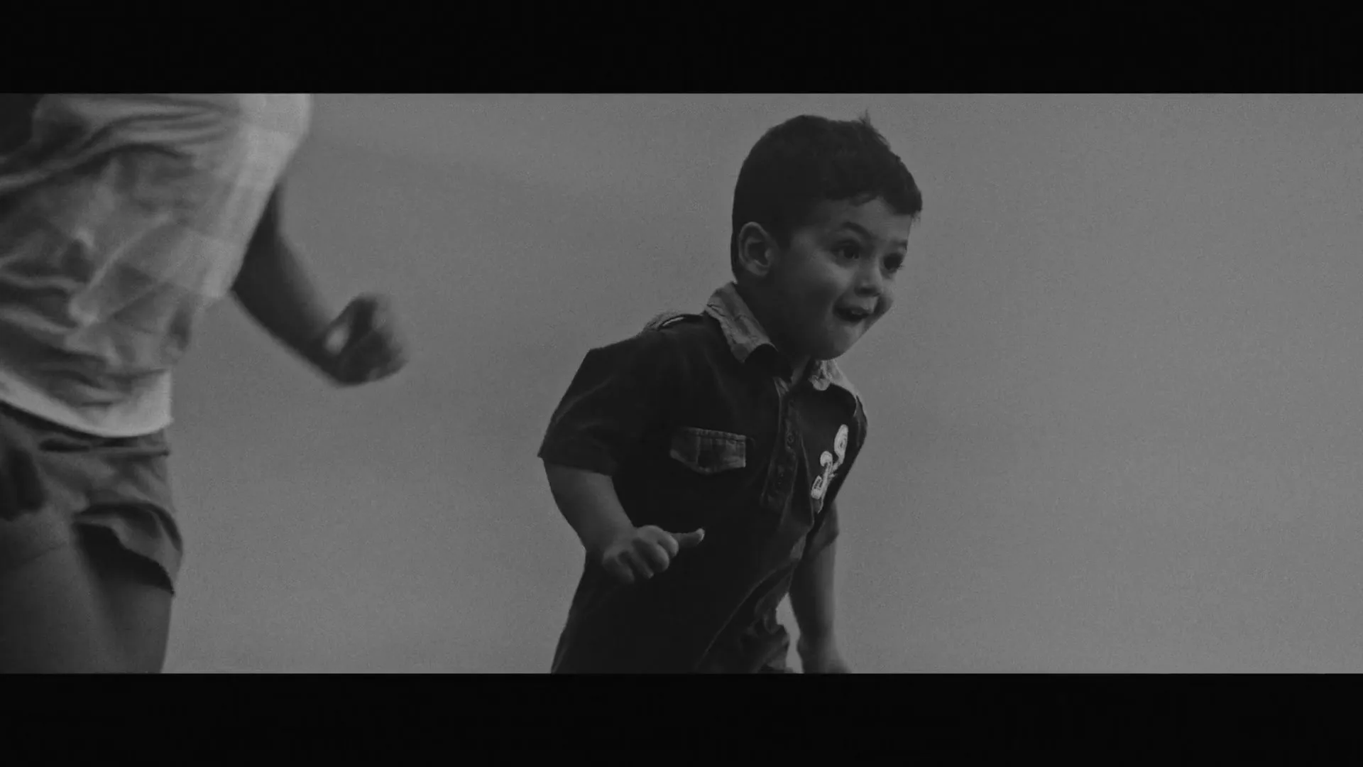 A young boy with dark hair and a polo shirt runs happily, looking to the right, with an adult's arm visible on the left.