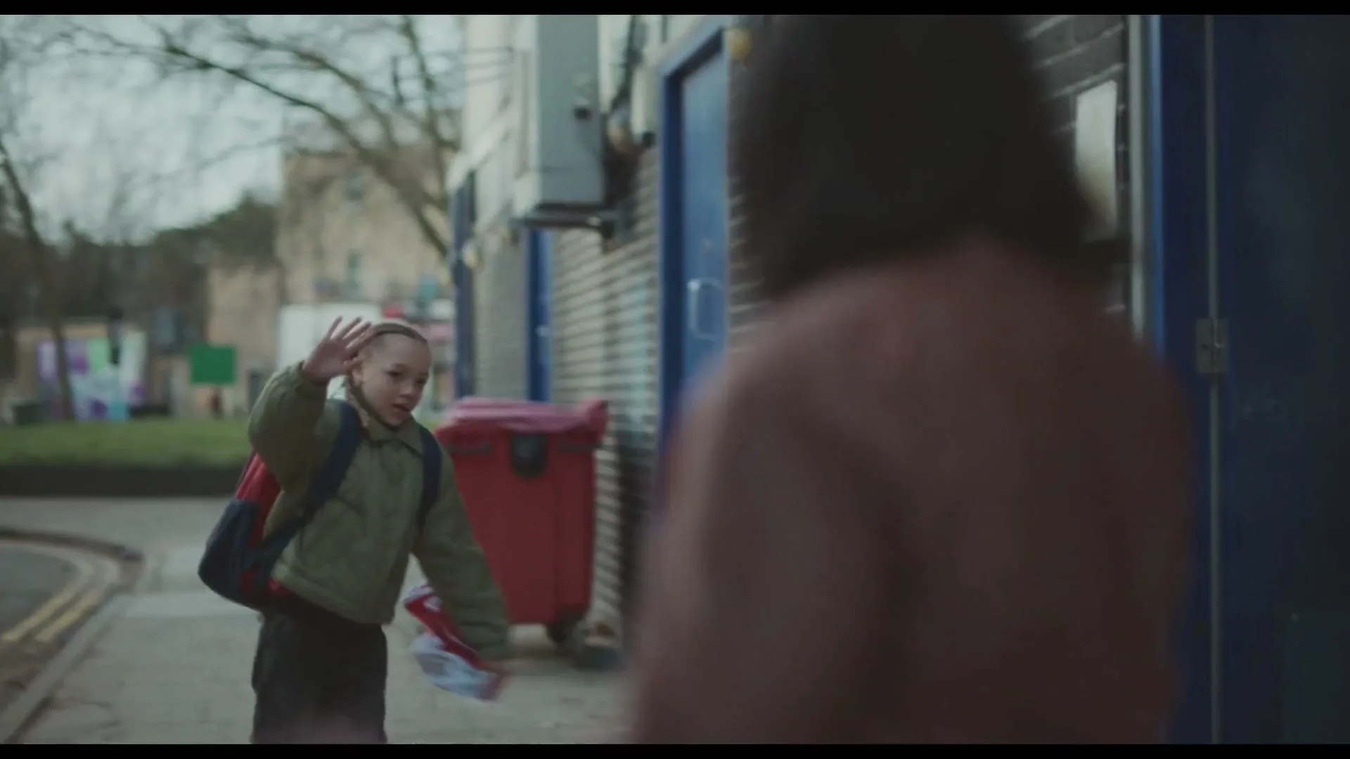 A woman talks on the phone, then a child runs past her and waves, as the camera pans to follow the child.