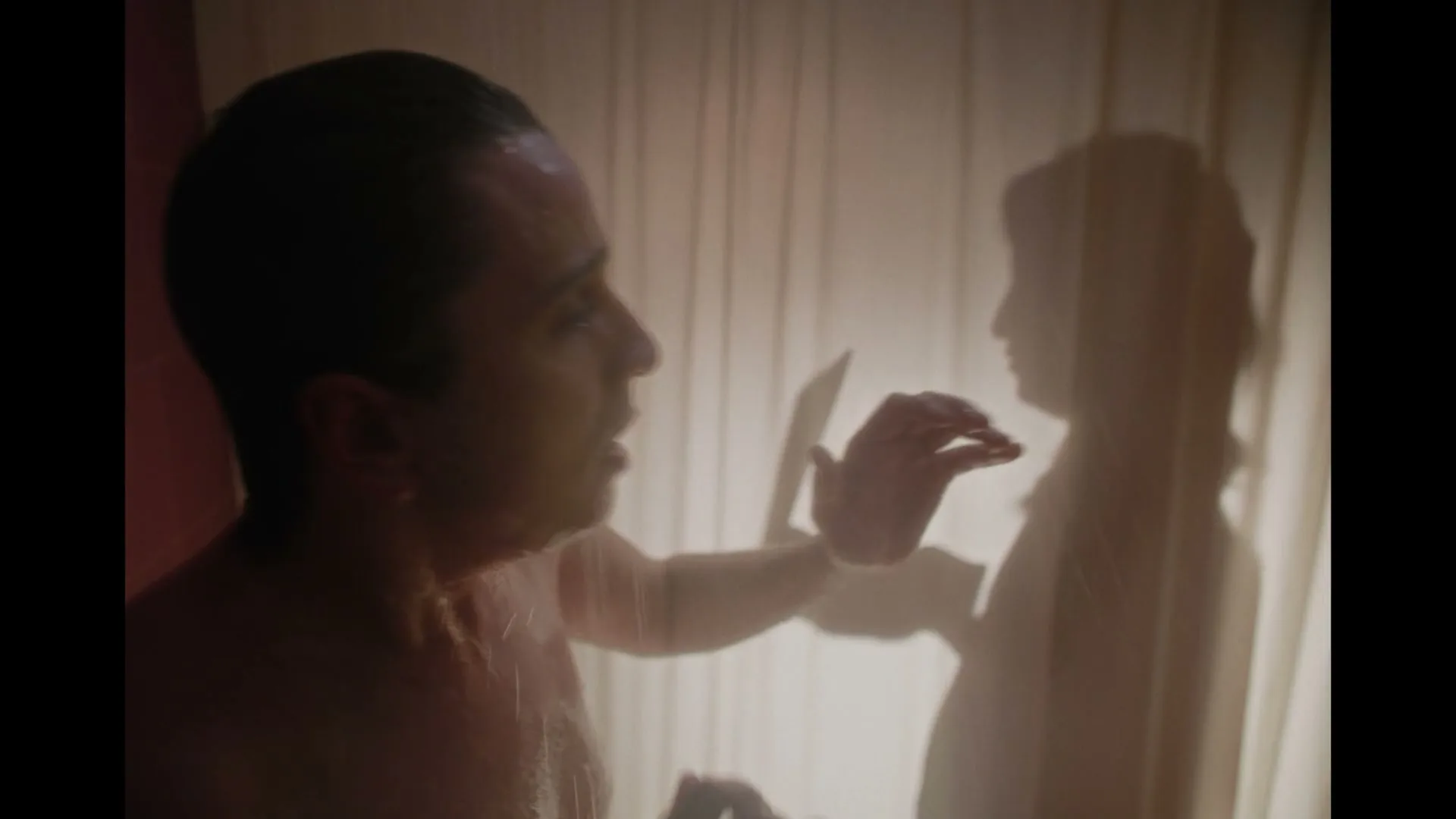 A man showers, looking at the silhouette of a woman behind a shower curtain, as if talking to her.