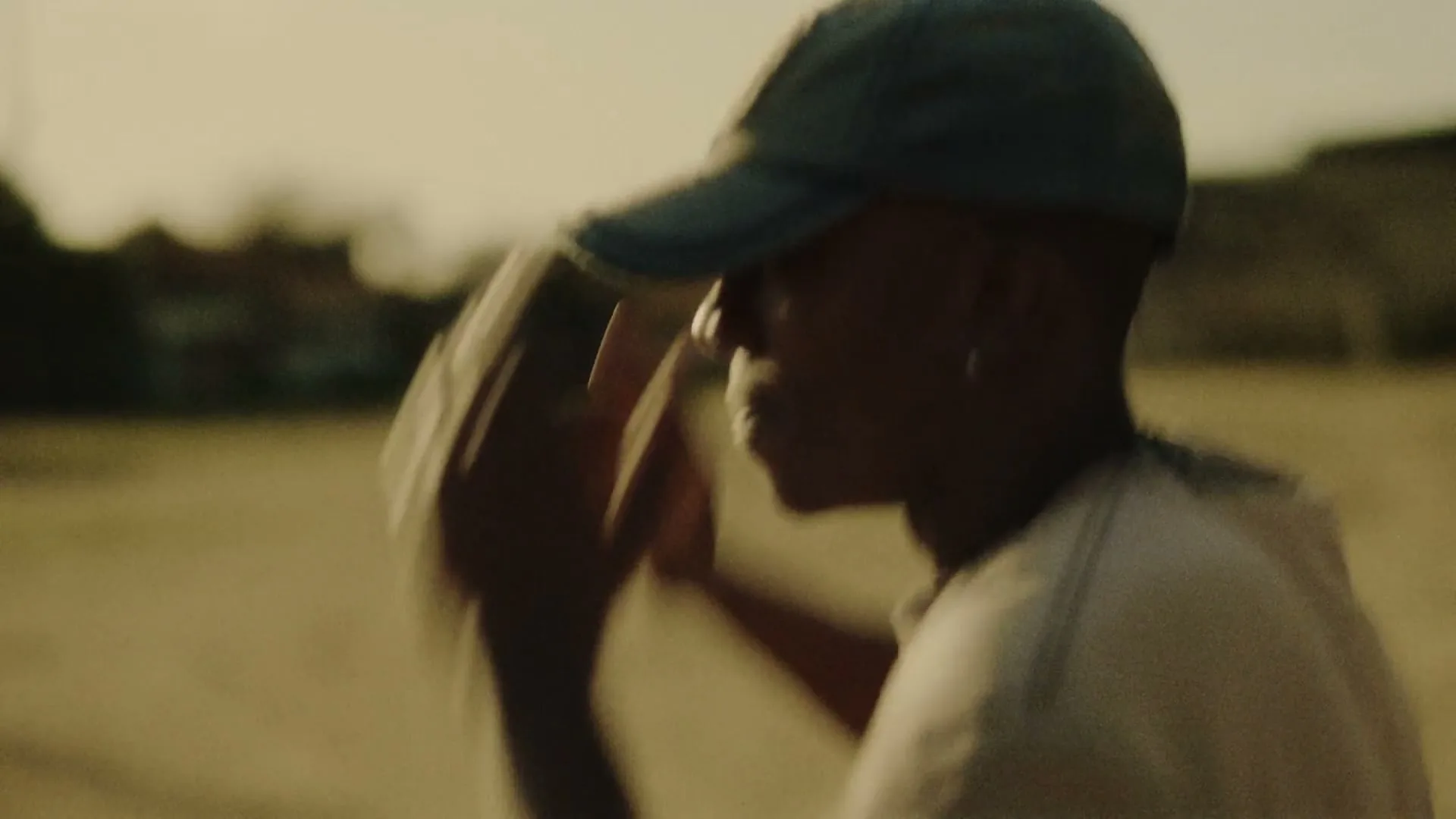 A young male baseball player in a cap and an older male coach talk on a dusty field at golden hour.