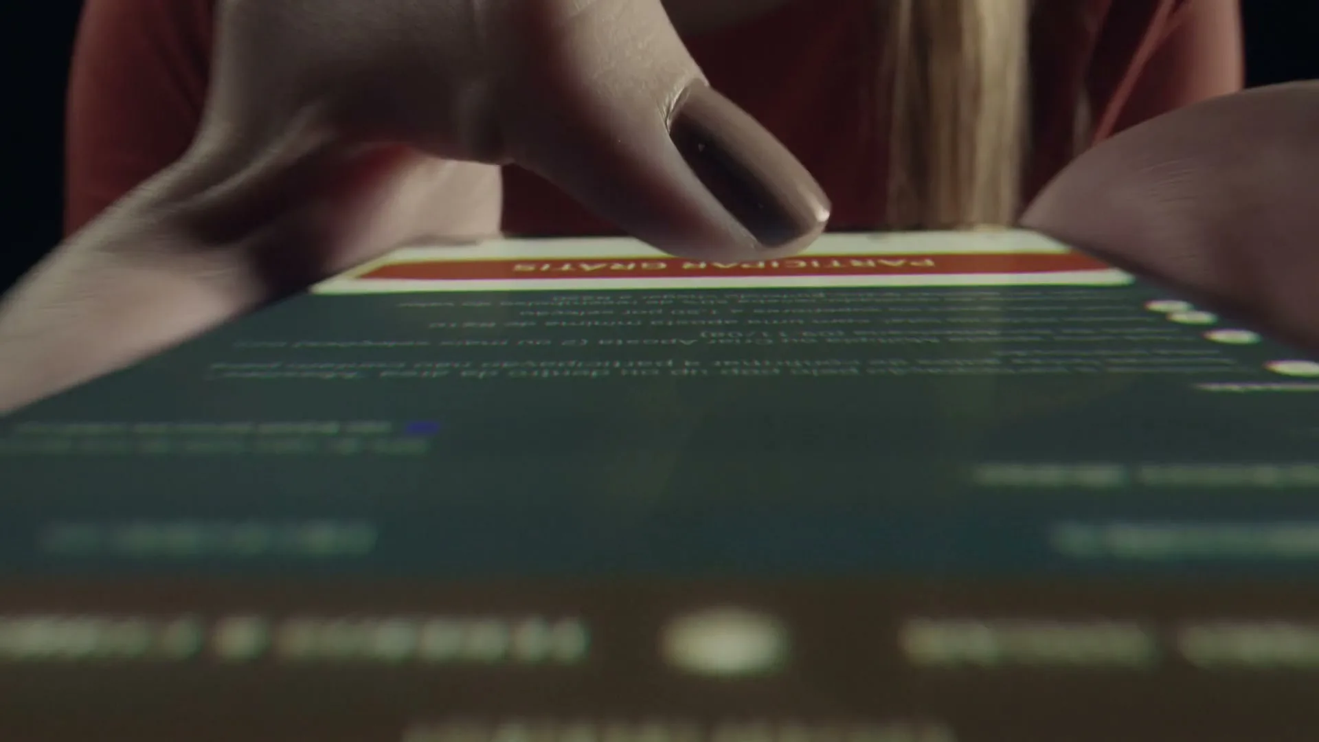 A woman's hands with painted nails tap on a smartphone screen, which displays text and a red button, in a close-up shot.