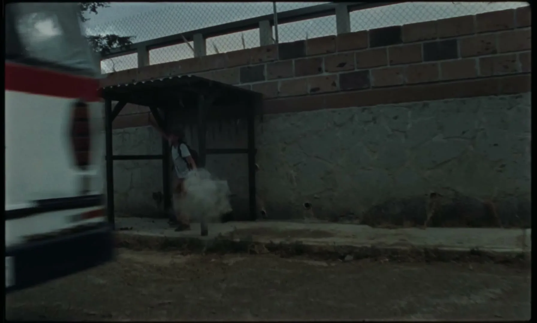 A child with a backpack runs to a bus stop shelter as a bus drives past, then sits down, looking distressed.