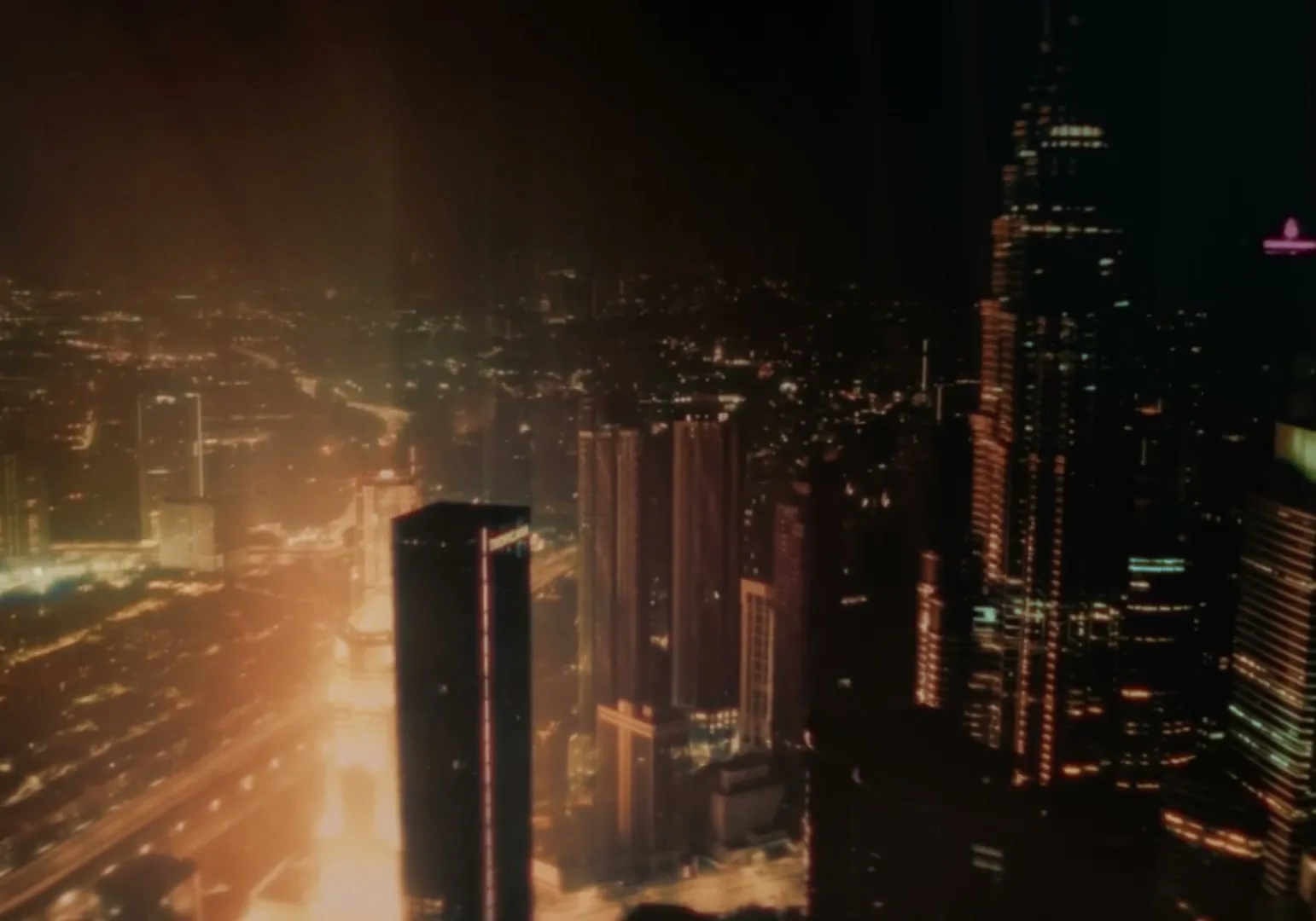 An aerial view of a city at night, with tall buildings and illuminated streets stretching into the distance under a dark sky.
