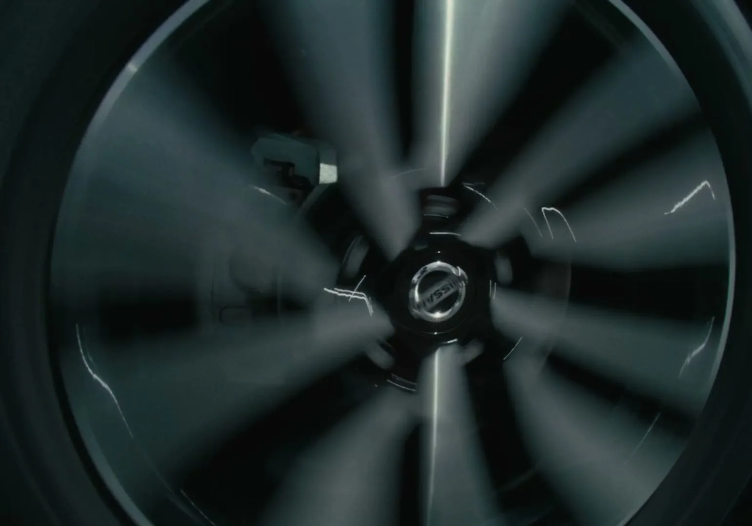 A Nissan car wheel with a visible logo spins rapidly, creating a blurred effect, as colorful lights flash behind it in a dark setting.