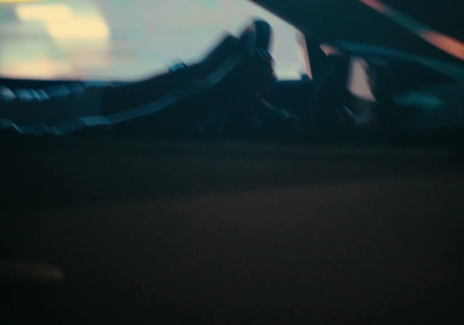 A blurry, dark shot of a car's interior, possibly the dashboard or seats, with a hint of light in the background.