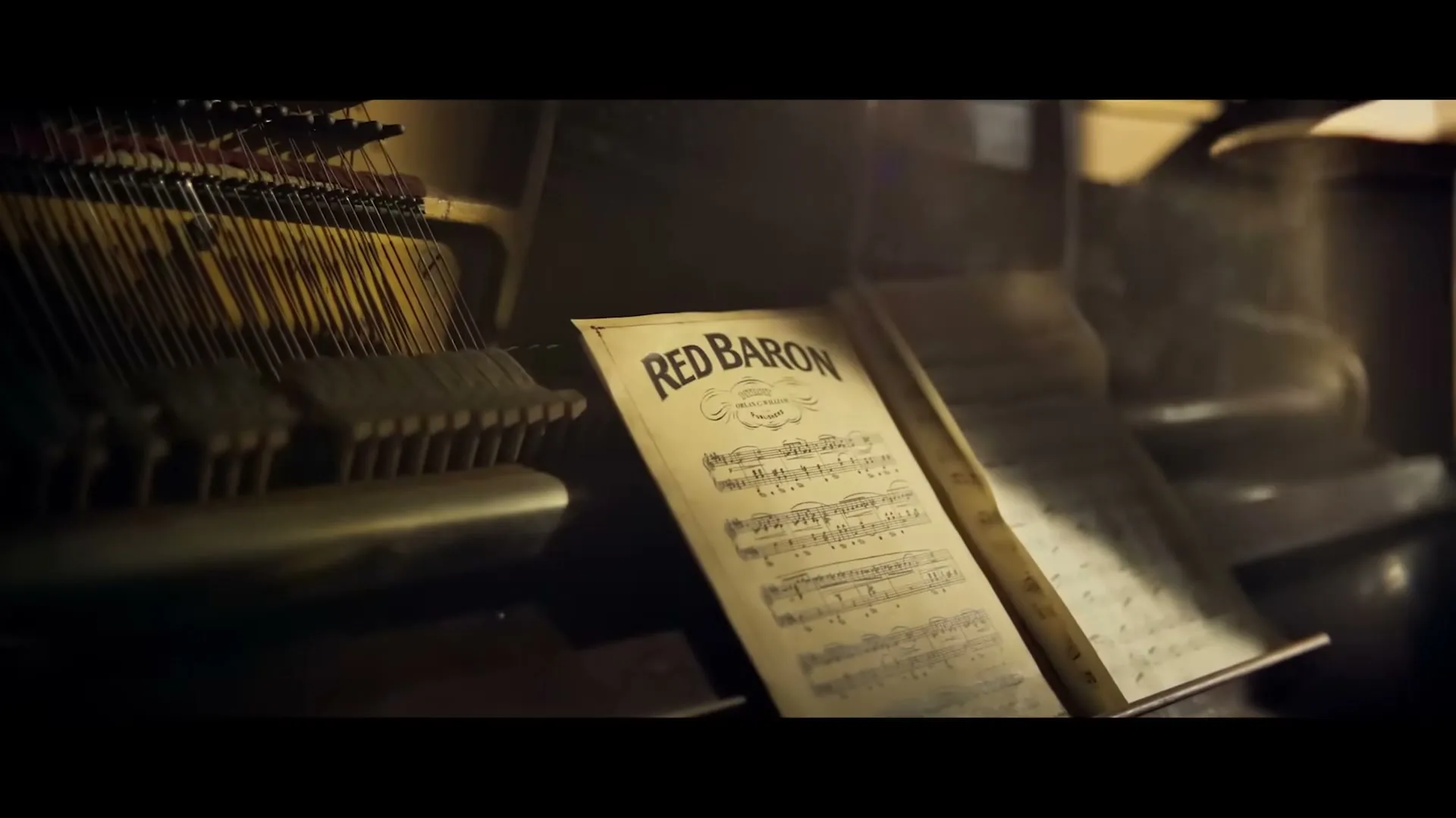 A close-up shot of an old, open piano with sheet music titled "Red Baron" on the stand, in a dimly lit room.
