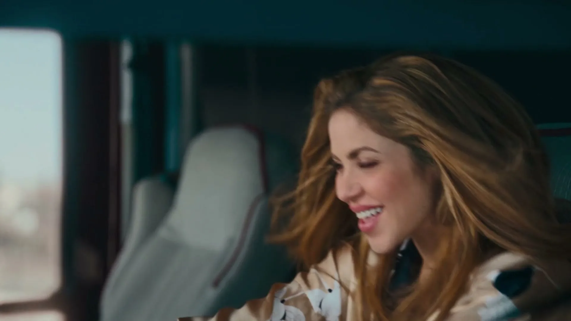 A woman with long blonde hair smiles happily as potato chips fly around her inside a vehicle.