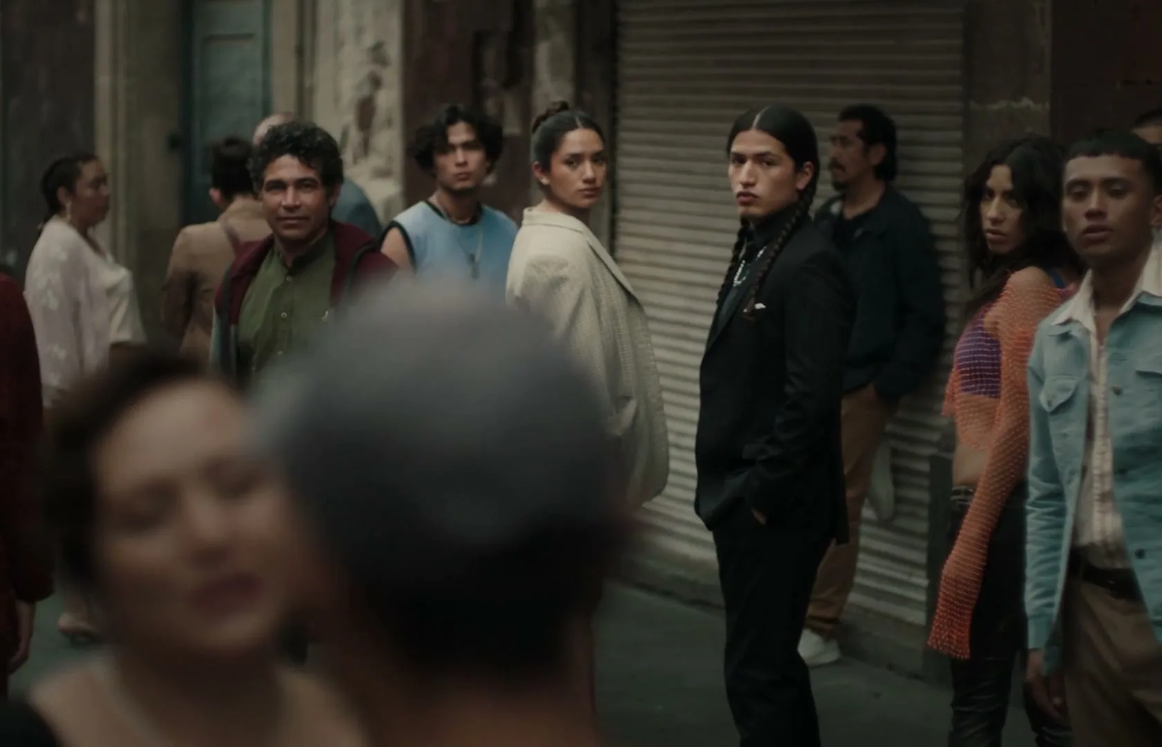 A diverse group of people, including a man in a suit and a woman in a blazer, stand on a busy city street, looking around.