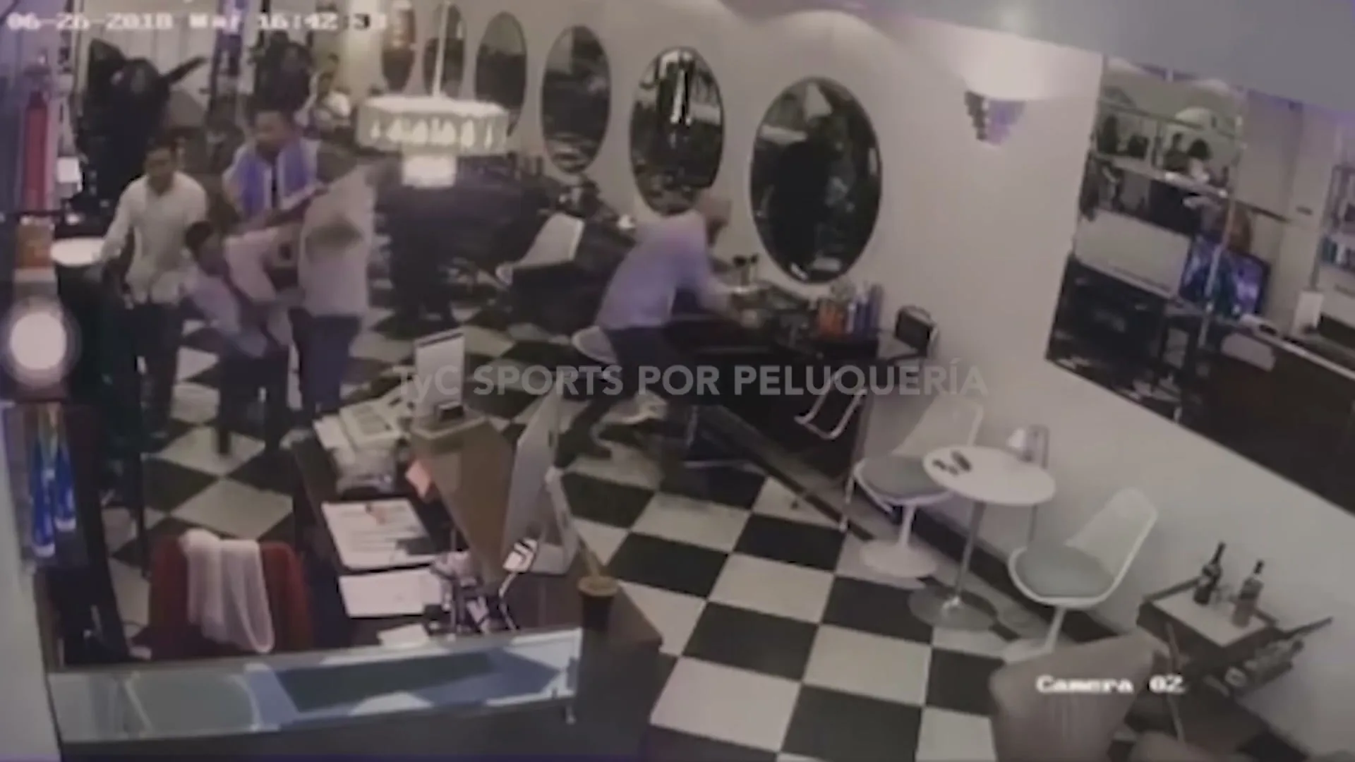 A security camera captures a group of men in a barbershop reacting excitedly to a soccer game, jumping and hugging each other.