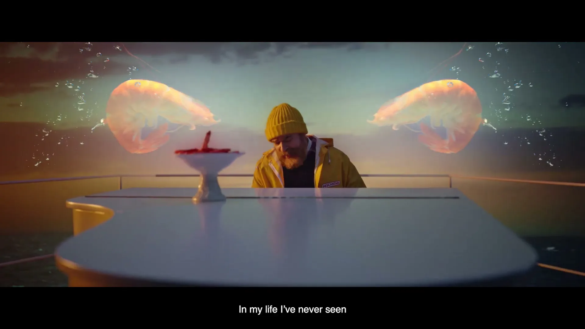 A bearded man in a yellow beanie and jacket sits at a white table on a boat, looking at a bowl of red shrimp, with two large, glowing shrimp appearing beside him.