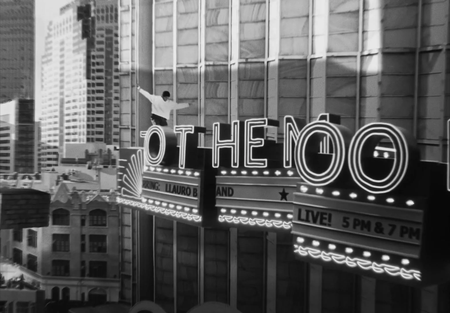 A young man in a white shirt balances on a large neon sign that reads "TO THE MOON" on the side of a tall building in a city.