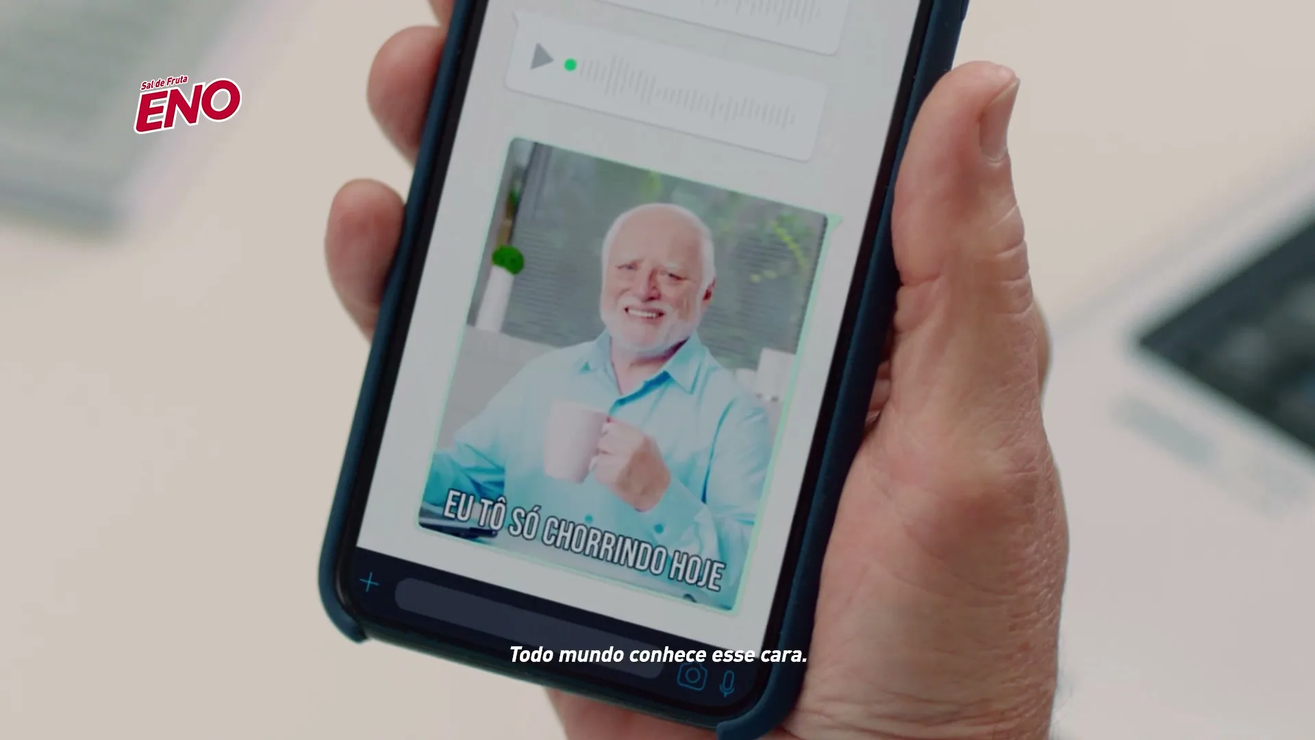 A person's hand holds a smartphone displaying a meme of an older man with a pained smile, with the Eno logo visible in the top left corner.