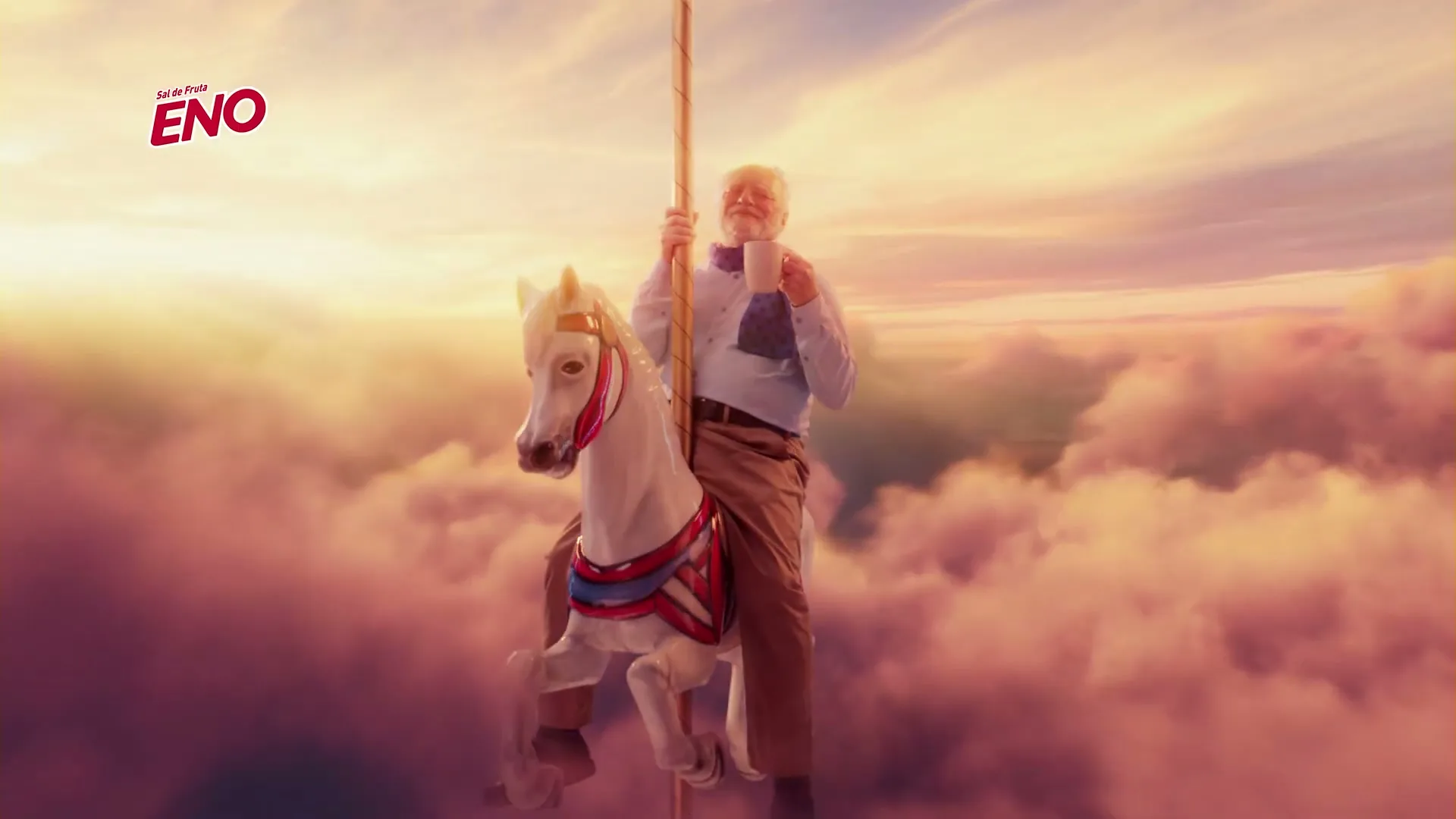 A senior man with a white beard, wearing a blue shirt and brown pants, rides a white carousel horse in the clouds, holding a white mug.