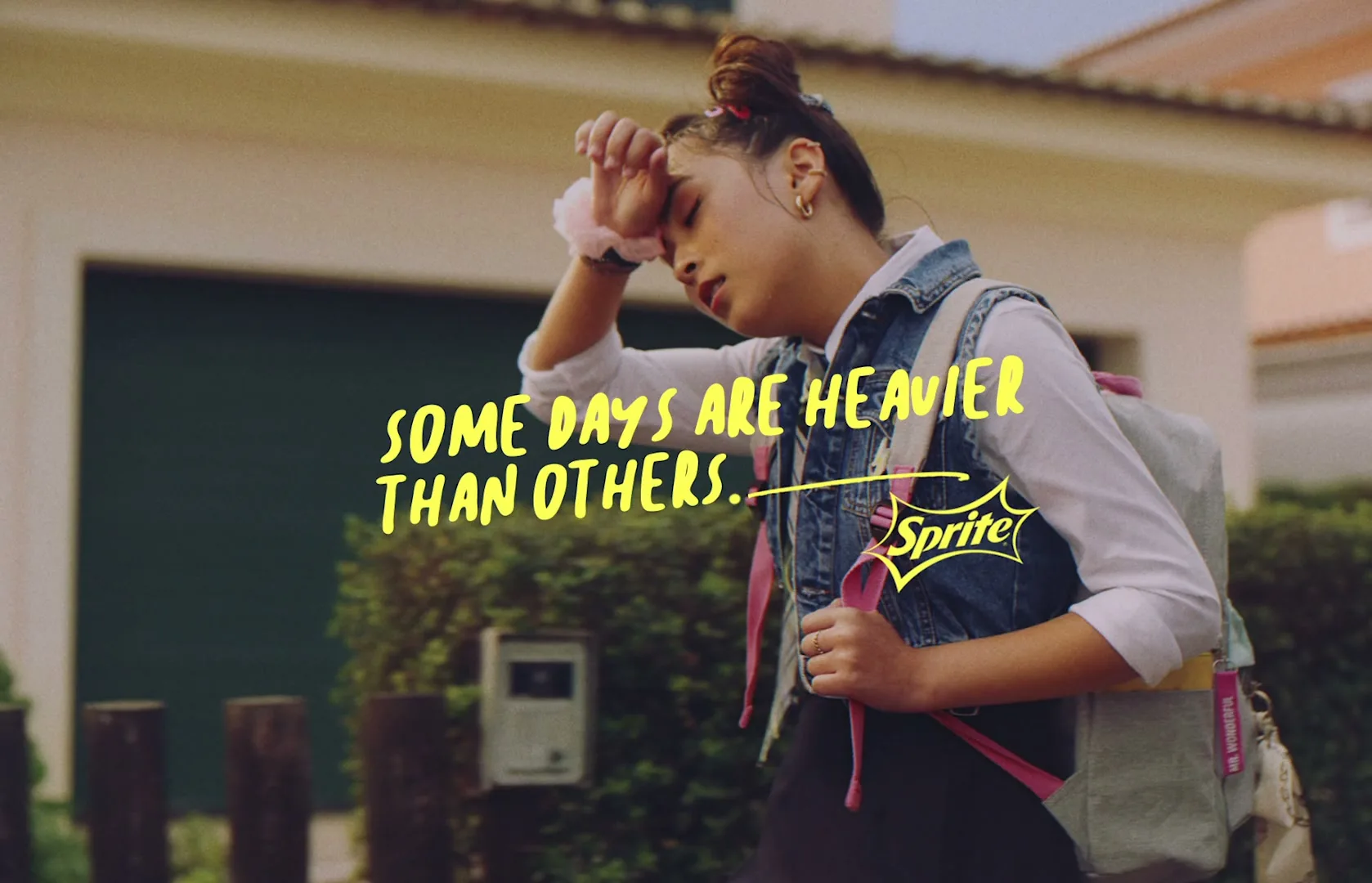 A tired teen girl with a backpack walks past a house, wiping her forehead, with text overlayed on the screen.