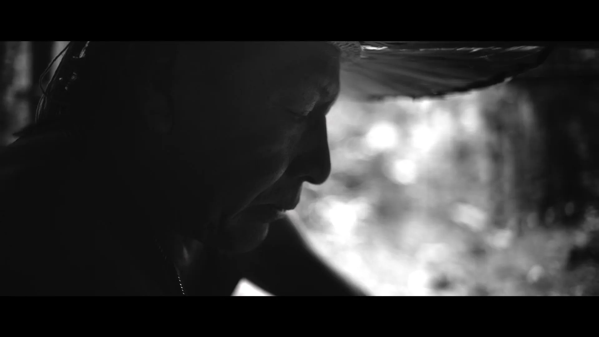 A man with a straw hat is seen in profile, looking down, with a blurred background of light, in a black and white shot.