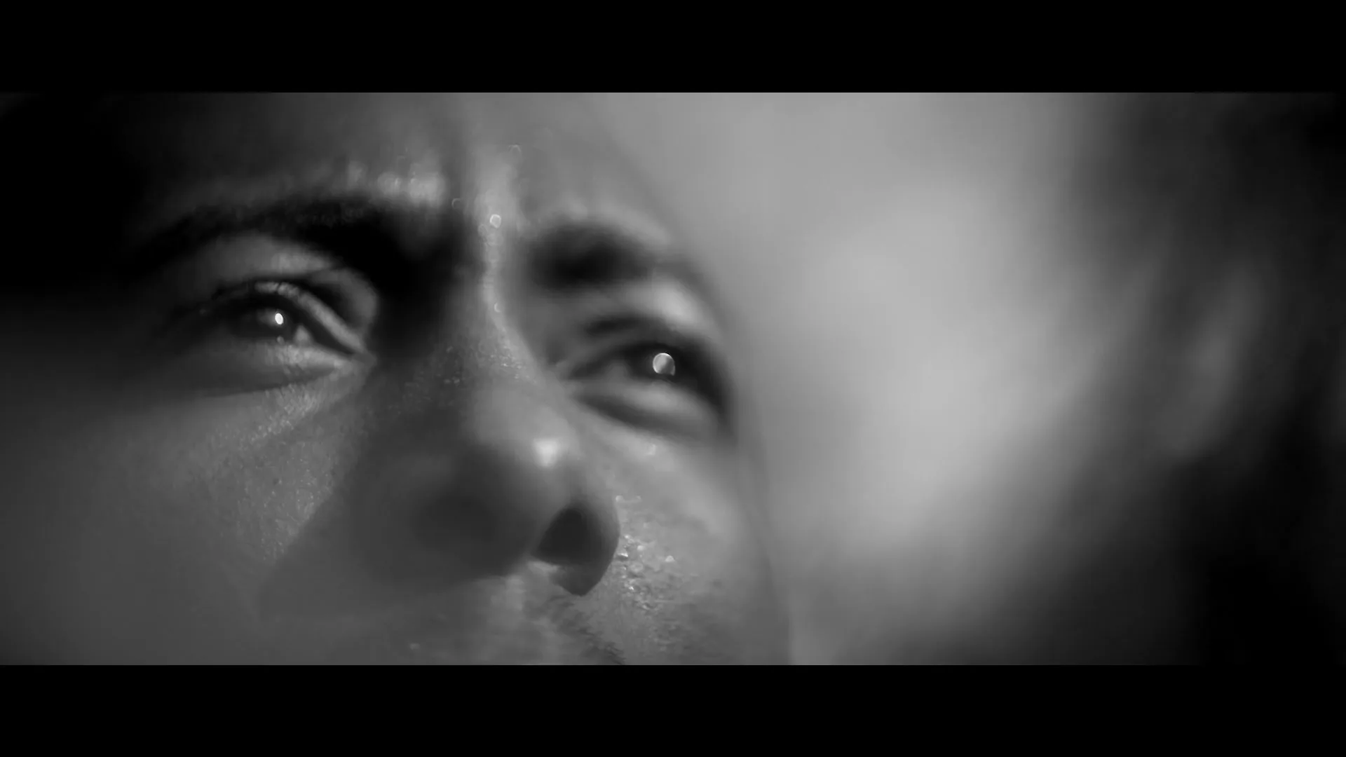A man's face, wet with sweat or water, is shown in a black and white extreme closeup, looking upwards with a serious expression.