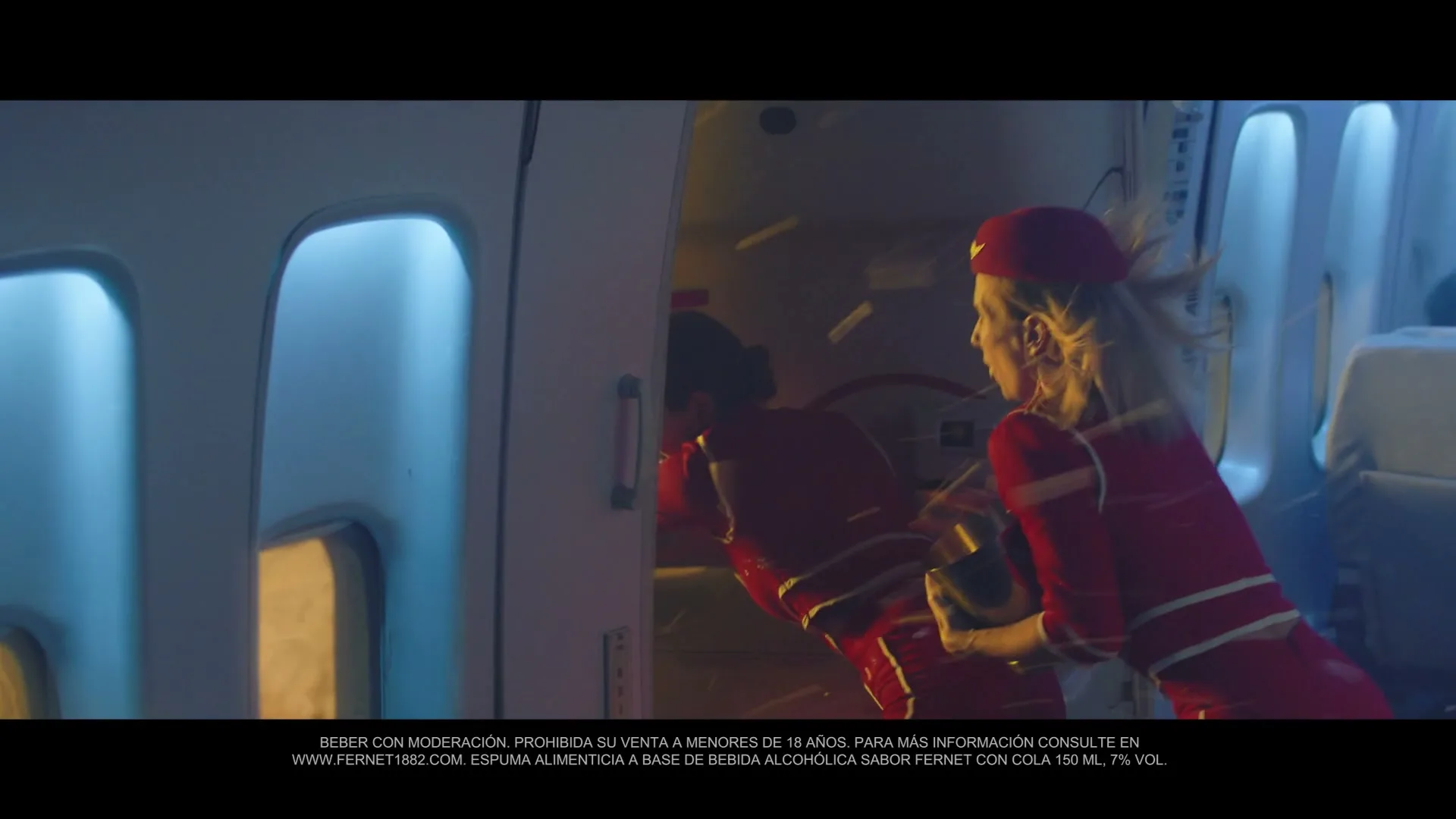 Two female flight attendants in red uniforms struggle to close an airplane door during a turbulent flight, with passengers visible in the background.