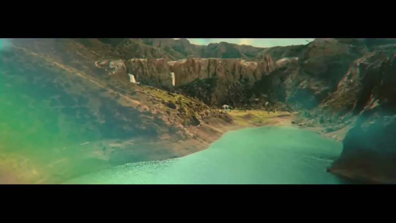 An aerial shot reveals a stunning natural landscape with a turquoise lake nestled among rugged mountains and a small waterfall.