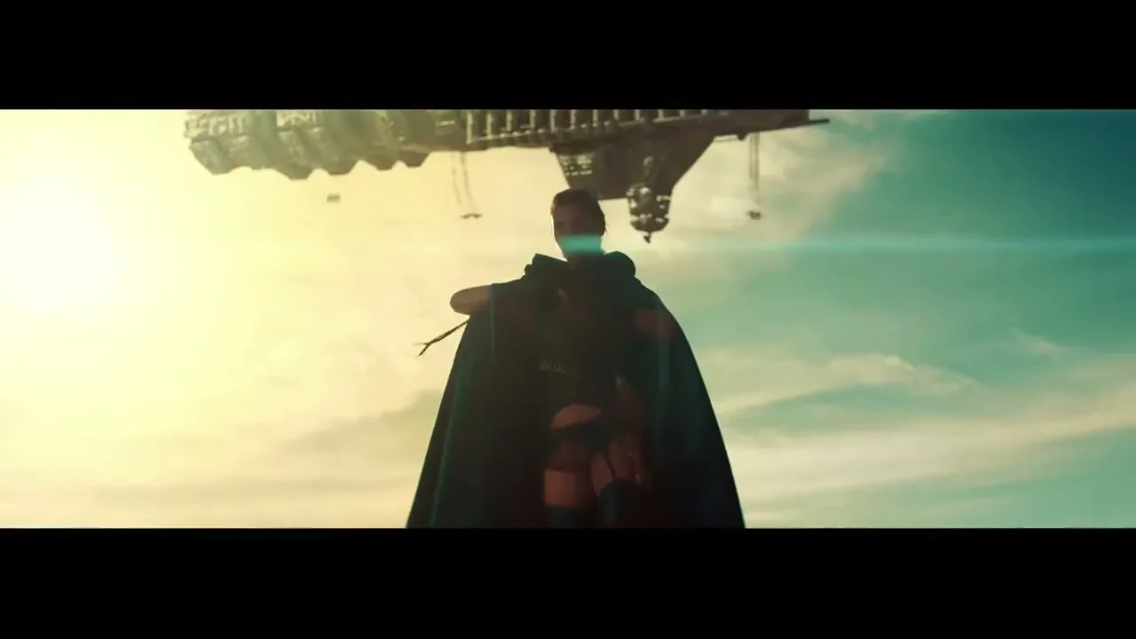 A female superhero in a dark cape stands with her back to the camera, looking up at a large spaceship in a bright, hazy sky.
