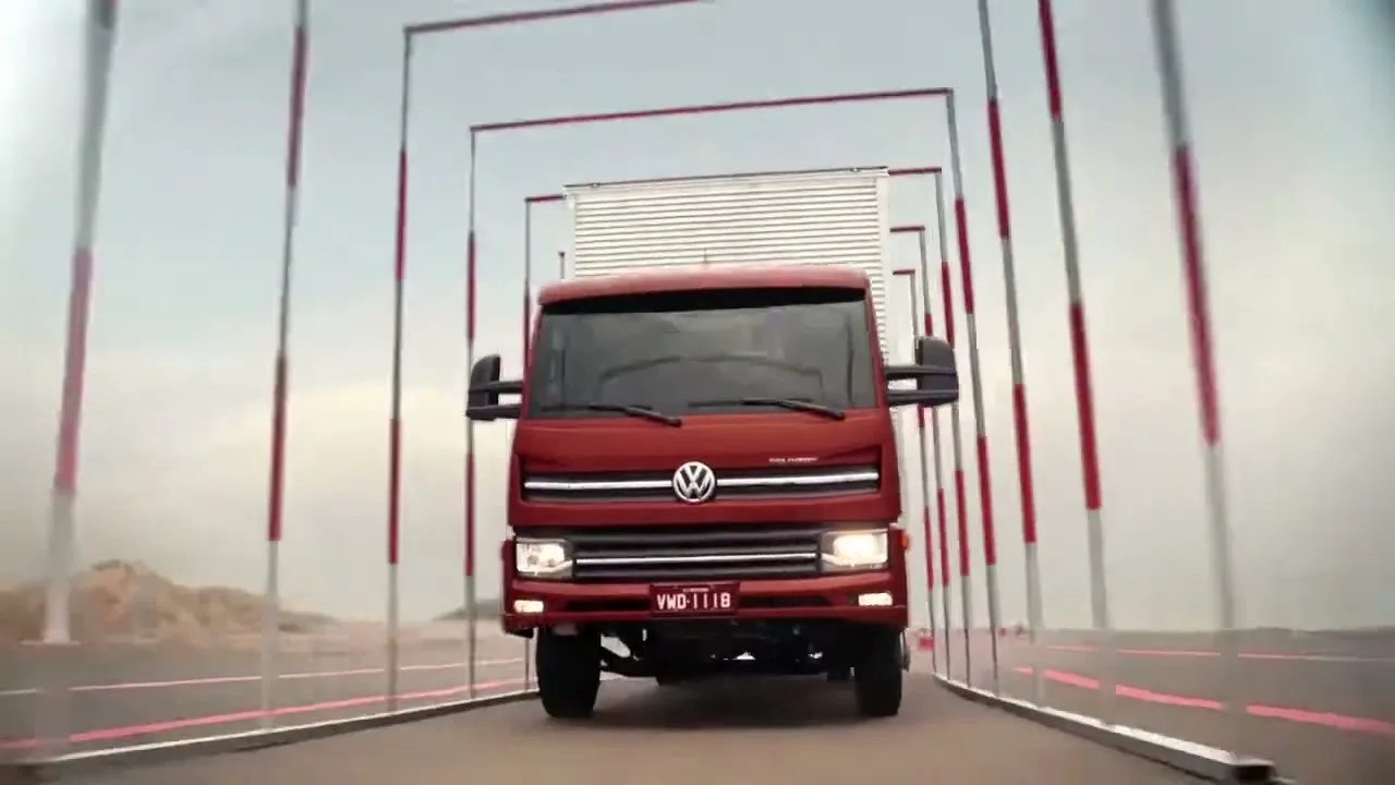 A red Volkswagen truck drives towards the camera on a test track, passing through a series of square frames under an overcast sky.