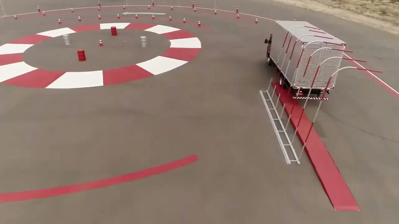 An aerial view shows a Volkswagen truck driving through a red and white striped obstacle course on a paved test track during the day.