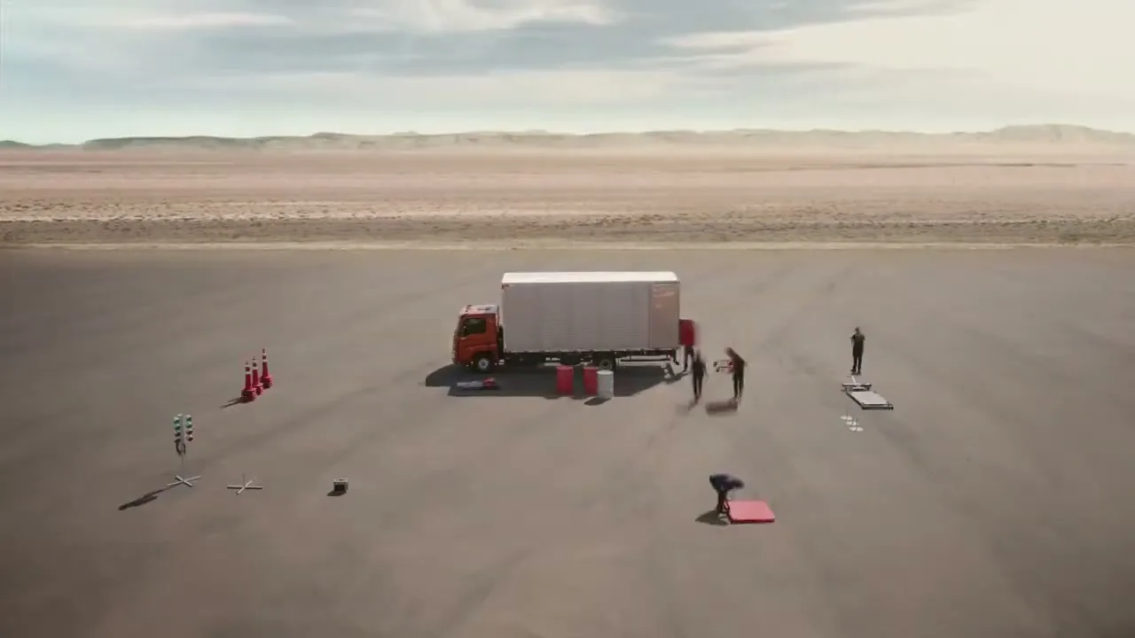 A Volkswagen truck is parked on a vast, empty desert plain, as a group of people quickly assemble a test track around it.
