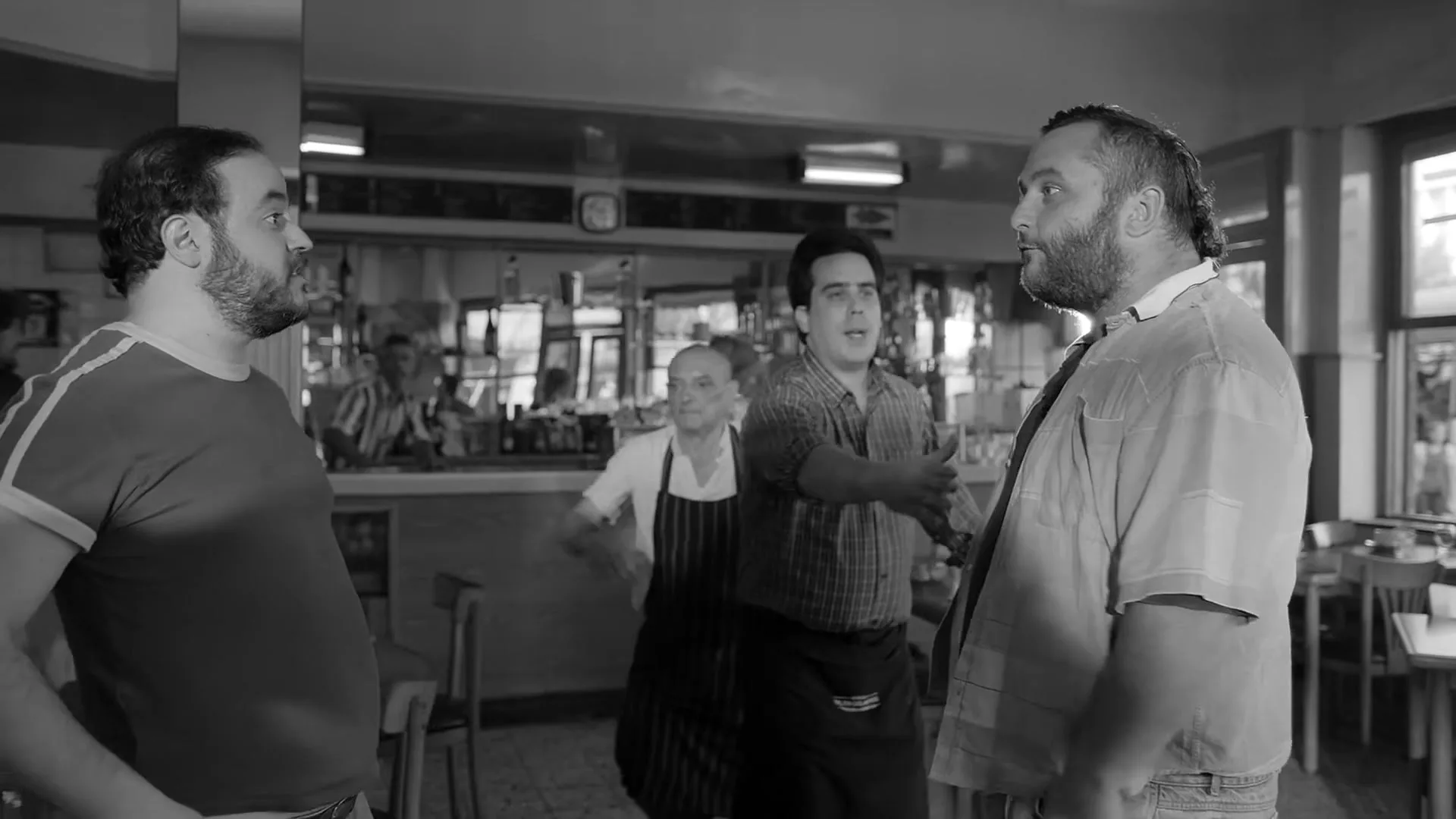 Two men argue in a diner, while a waiter tries to intervene and another man watches from the background.